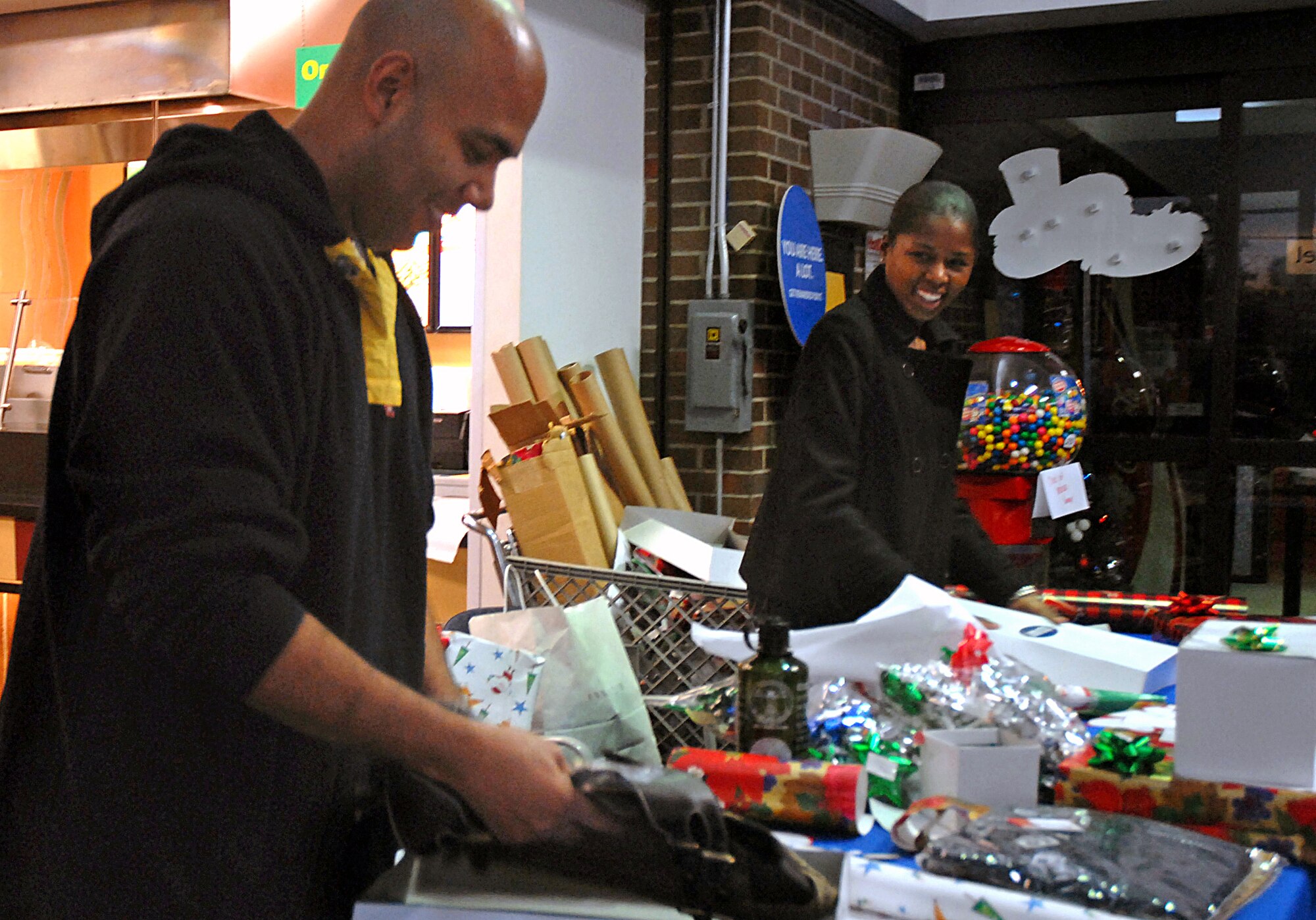 Tech. Sgt. Elliot Reed, 437th Airlift Wing Safety Office and Staff Sgt. Stephanie Scott, 437 AW Legal Office, volunteered at the Charleston AFB Exchange to wrap presents for BX patrons Monday. Both volunteered to wrap presents to raise money for the Airlift Wing Booster Club. (U.S. Air Force photo/Tech. Sgt. Paul Kilgallon)
