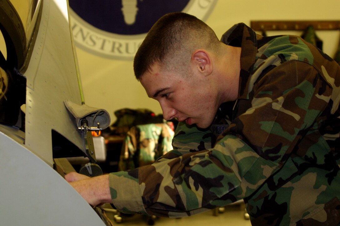 Airman Tyler Pier, an Airman in Training at the 361st Trianing Squadron, and his father, Master Sgt. Brett Pier,  a retrainee at the 364th TRS, have the opportunity to be part of something unique Dec. 20 when they both graduate from technical training. Airman Pier, securing a pin to a mock F-16 canopy, is training to be an egress apprentice, while Sergeant Pier is attending the cable and antenna systems course. (U.S. Air Force photo/John Ingle)