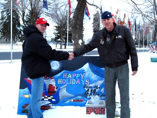 Col. Gary Batinich, 419th Fighter Wing commander, shakes hands with Staff Sgt. Luke Munk in front of the wing's holiday greeting card displayed near the South Gate. Sergeant Munk, an Air Reserve Technician with the wing's Maintenance Squadron, designed and painted the card which took first place in a base-wide competition.  (U.S. Air Force Photo/Bryan Magaña)