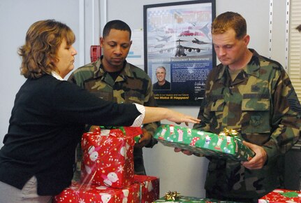 Faye Cook, Boeing manager for C-17 spares support, presents donated gifts to Master Sgt. Kendrick Mast, 437th Aerial Port Squadron first sergeant, and Master Sgt. Thomas McGowan, 17th Airlift Squadron first sergeant, Dec. 13.  Employees from the Boeing Company collected more than 25 gifts for the Holiday Cheer/Angel Tree Program. (U.S. Air Force photo/Staff Sgt. Jennifer Arredondo)