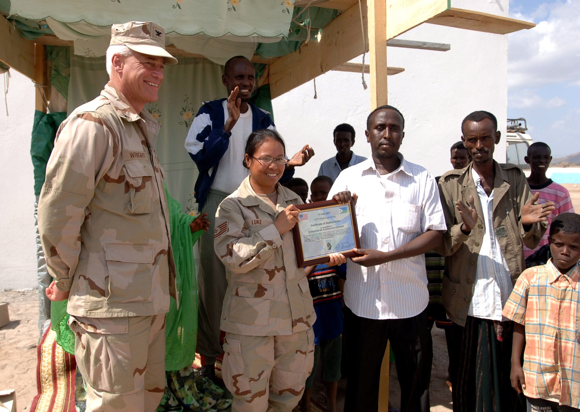 Navy Capt. Bob Wright, (left to right)  looks on as Tech. Sgt. Marrisa Luke presents a certificate of appreciation to the owner of Enterprise De Construction Go Baad for a job well done following the dedication ceremony Dec. 17 in Djibouti. Captain Wright is the Combined Joint Task Force-Horn of Africa J-9 Strategic Communications director, and Sergeant Luke is a CJTF-HOA engineer. (U.S. Navy photo/Petty Officer 1st Class Mary Popejoy) 
