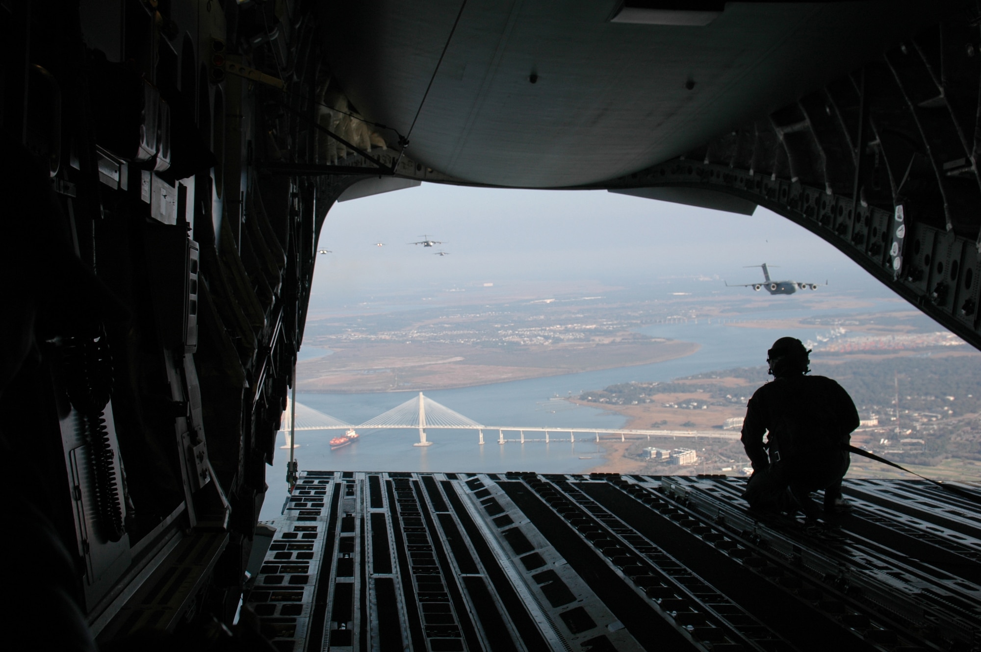 Senior Airman Josh Fugle, loadmaster, 701st Airlift Squadron, watches C-17s from the ramp of a Globemaster III as they fly over the Arthur Revenal Bridge in Chalreston, SC Dec. 20. The flight was part of a 15-ship formation flown by active duty and Reserve squadrons from Charleston AFB, SC. Thirty-five employers and civic leaders from the Charleston area rode along with the 315 AW, in the formation and witnessed airdrops and air refuelings. (Photo by Capt. Wayne Capps, USAFR)
