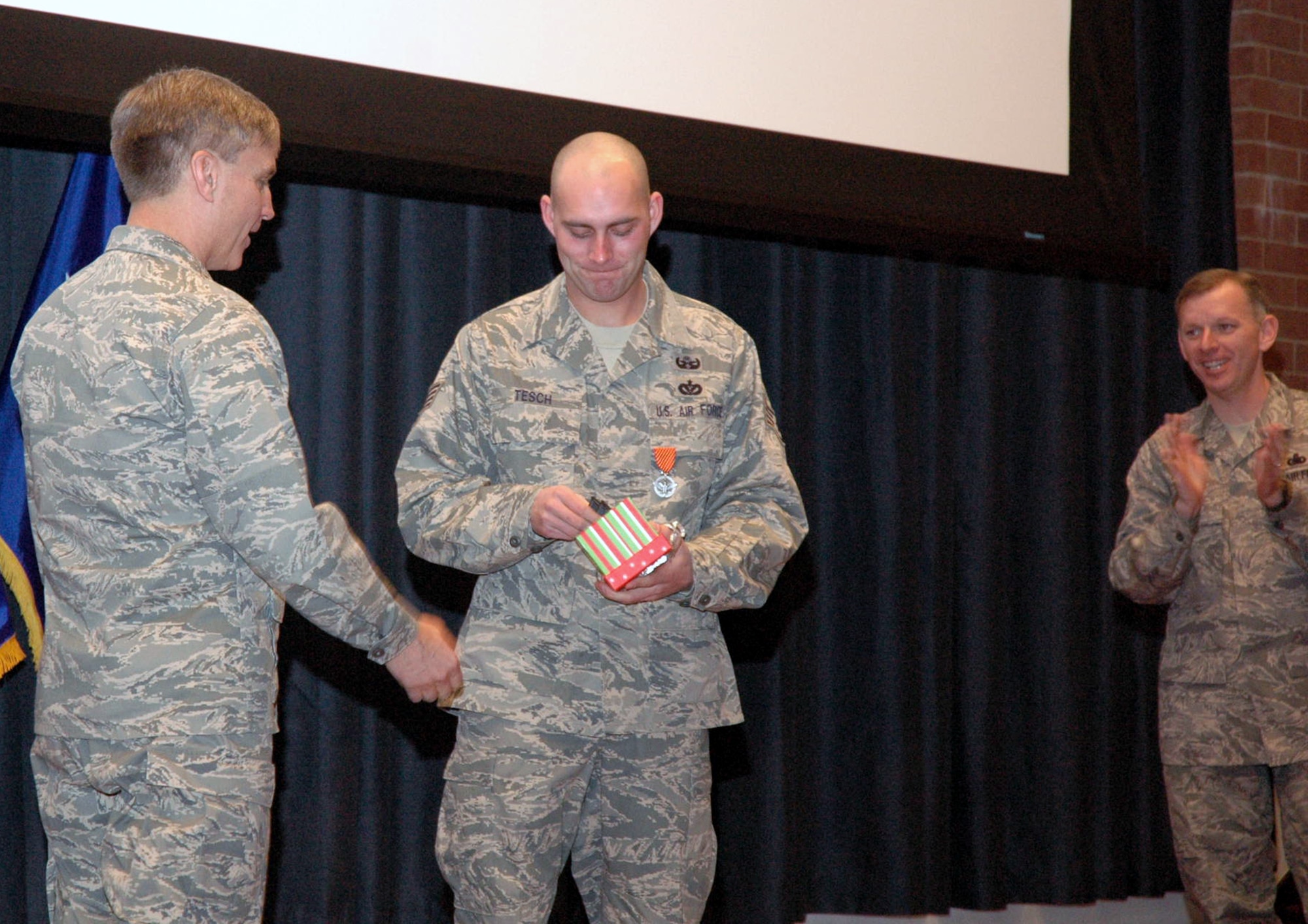Newly promoted Tech. Sgt. Michael Tesch, explosive ordnance disposal craftsman with the U.S. Air Force Expeditionary Center's 421st Combat Training Squadron, opens a gift box with new technical sergeant stripes from Maj. Gen. Kip Self, USAF EC commander.  Sergeant Tesch received his new rank through the Stripes for Exceptional Performers, or STEP,  program.  During the commander's call, Sergeant Tesch was also presented with the Air Force Combat Action Badge. Cheering the promotion is Chief Master Sgt. Jeffry Helm, USAF EC command chief.  (U.S. Air Force Photo/Tech. Sgt. Scott T. Sturkol)