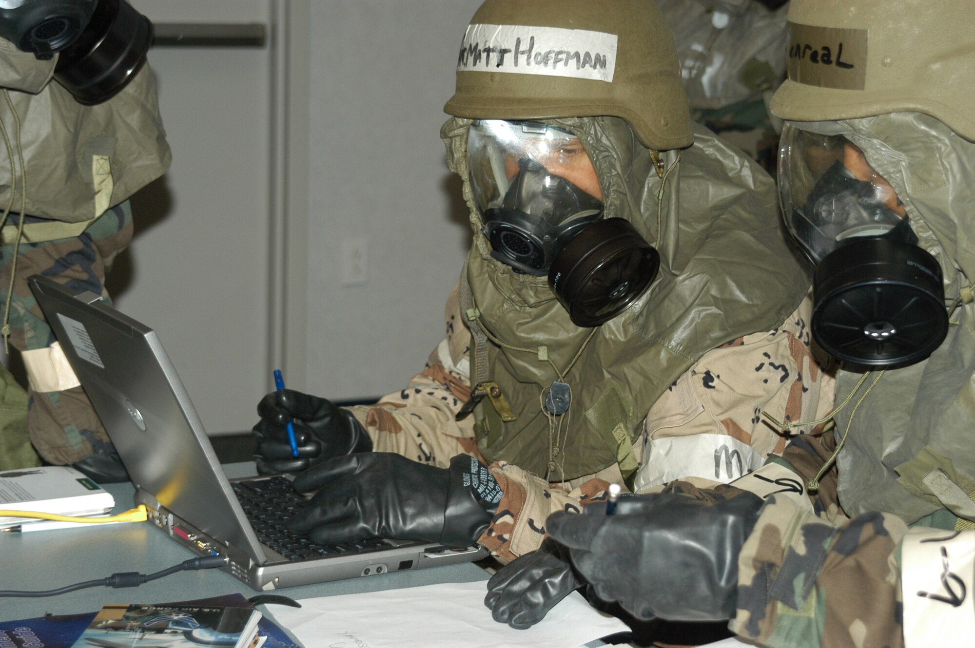 (left to right) Capt. Hoffman, 301st Mission Support Squadron, practices typing in MOPP Level-4 during a recent Enemy Attack Exercise. 301st Fighter Wing members used this opportunity to pratice routine tasks in complete chemical ensemble. Capt. Marc Monreal (right), 301st Mission Support Group executive officer, gives the old fashion methon of pen and paper a go. (U.S. Air Force Photo/Staff Sgt. Kristin Mack)