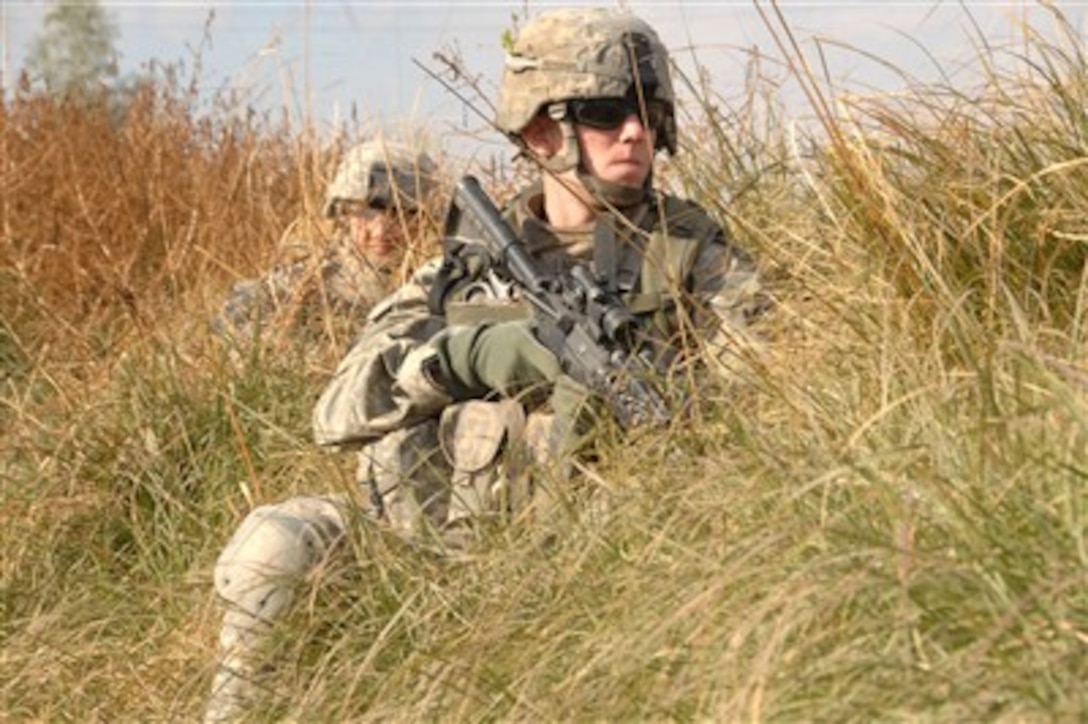 Two U.S. Army soldiers from Alpha Company, 2nd Battalion, 23rd Infantry Regiment, 4th Brigade Combat Team, 2nd Infantry Division take cover in tall grass on the side of the road during a patrol in Muqdadiyah, Iraq, on Dec. 19, 2007.  