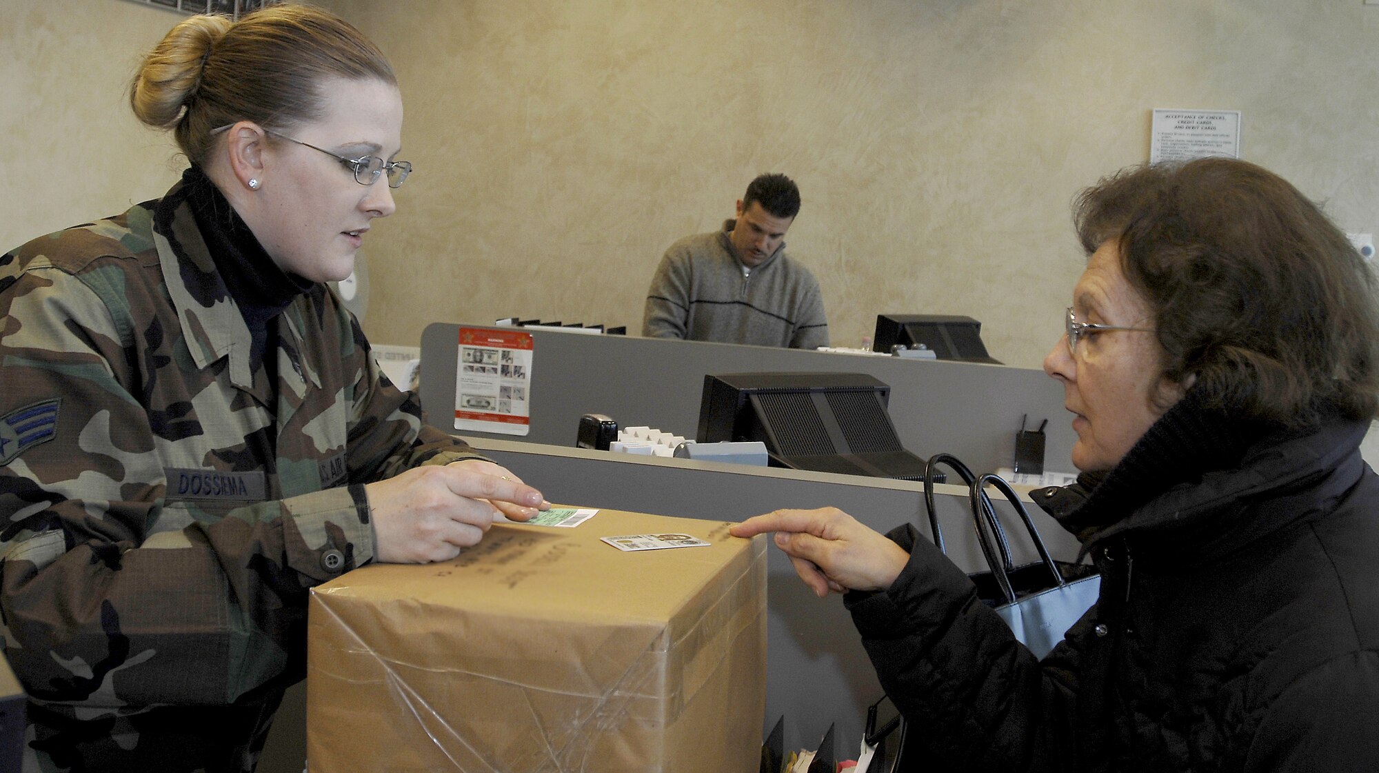 Senior Airman Tara Dossiema, 31st Communications Squadron postal clerk, left, checks an ID card as she helps a customer mail out a package Jan. 25.    (Photo by Airman 1st Class Liliana Moreno)