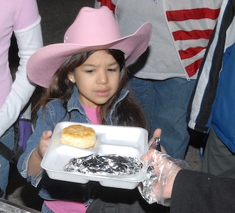 Laura Gutierrez, 6, a Lackland Elementary School first-grader, is handed an egg, potato and cheese taco and a biscuit Jan. 26 during the 3rd Annual Lackland Independent School District Cowboy Breakfast. She is the daughter of Amanda and Staff Sgt. Victor Gutierrez of the Cryptologic Systems Group. Breakfast-goers chowed down on 500 tacos containing 45-dozen eggs, 500 biscuits, 350 servings of grits, hot chocolate, coffee and a variety of fruit juices. (USAF photo by Robbin Cresswell)