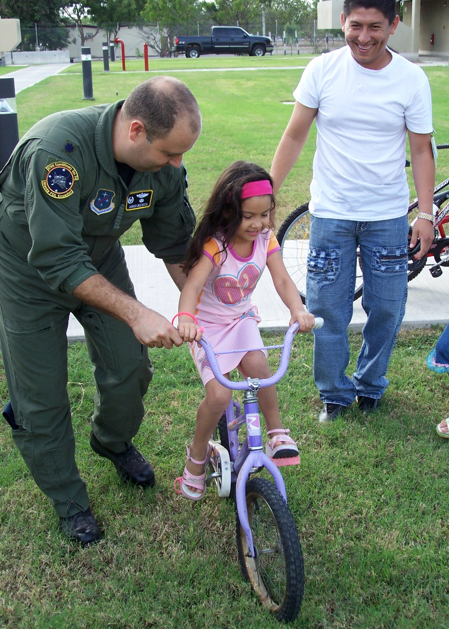 Lt. Col. Javier Delucca helps a girl try out her new bicycle while her father looks on.  (U.S. Air Force official photo)