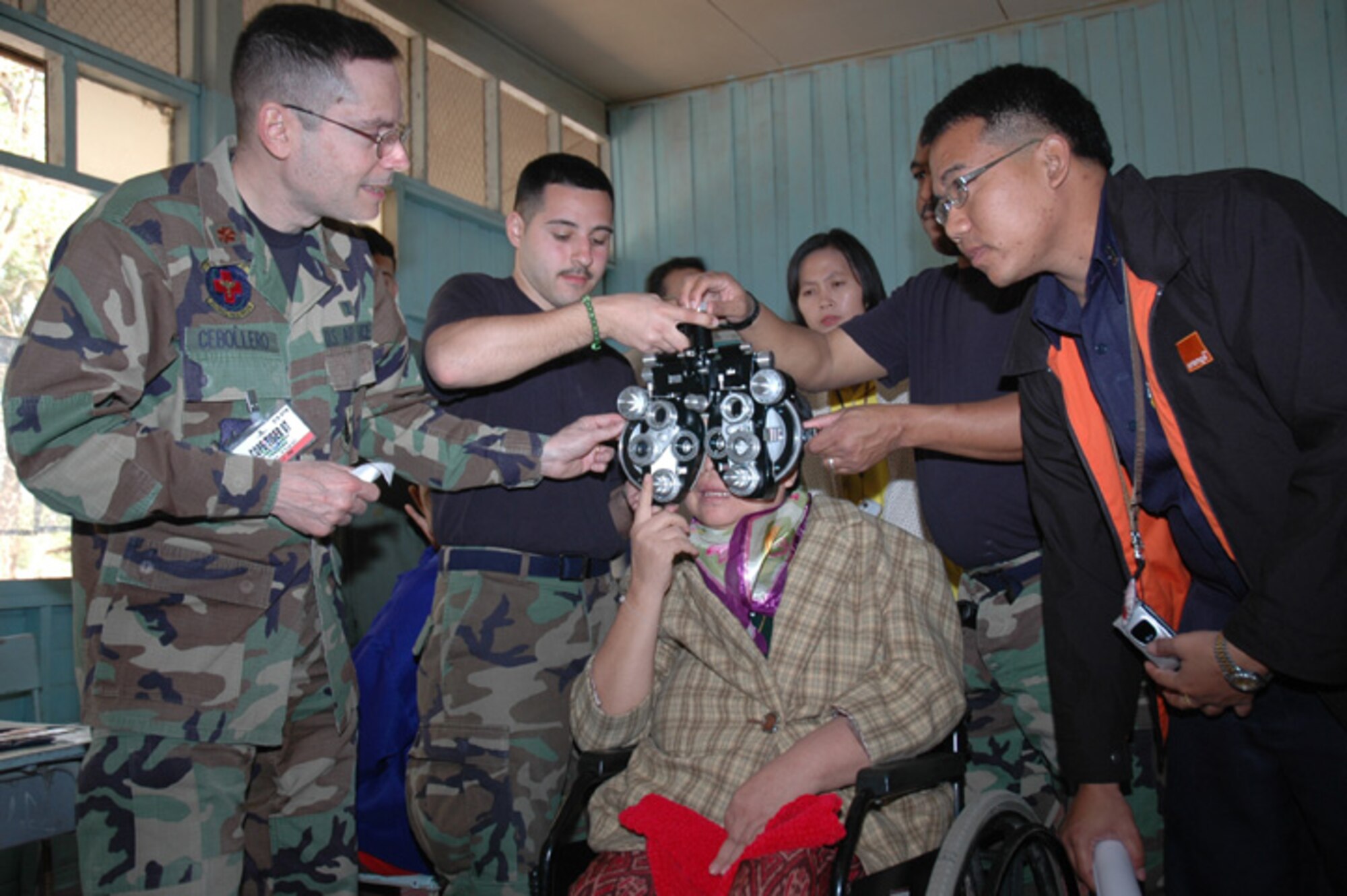 It’s a team effort to exam a wheel chair bound patient, as Senior Airman David Hernandez (L), 374th Aeromedical Dental Squadron, Yokota Air Base, Japan, and Tech. Sgt. Edward Hill (R), 18th Aeromedical Dental Squadron, Kadena Air Base, Japan hold the vision testing equipment in place as Maj. Carlos Cebollero, 374th AMDS, adjusts the settings  for the sharpest vision.  An interpreter awaits the opportunity to bridge the language barrier. (USAF photo by Staff Sgt. Betty Squatrito-Martin)