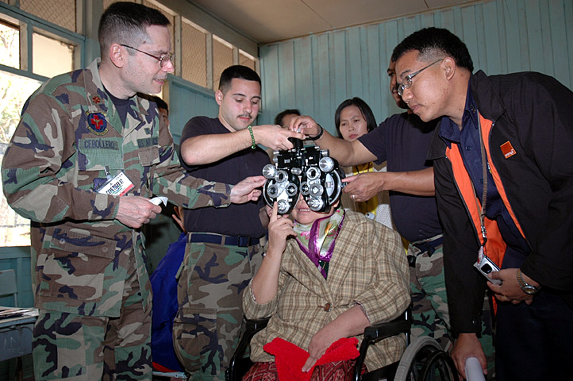 Maj. Carlos Cebollero adjusts the settings for the sharpest vision during an examination of a wheelchair-bound patient as Senior Airman David Hernandez and Tech. Sgt. Edward Hill hold the vision testing equipment in place as an interpreter listens closely Jan. 30 in Korat, Thailand. Airman Hernandez and Major Cebollero are assigned to the 374th Aeromedical Dental Squadron at Yokota Air Base, Japan, and Sergeant Hill is from the 18th Aeromedical Dental Squadron at Kadena AB, Japan. Military members from the United States, Thailand and Republic of Singapore took part in a humanitarian mission at the school as part of Exercise Cope Tiger 2007. (U.S. Air Force photo/Staff Sgt. Betty Squatrito-Martin) 

