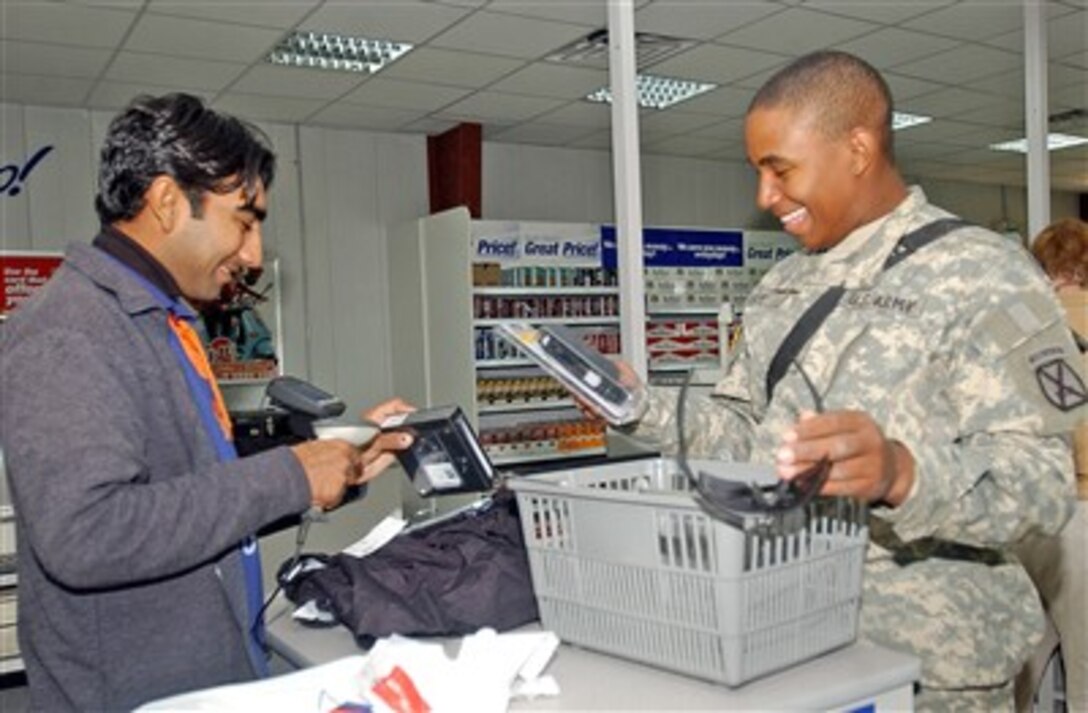 U.S. Army Pfc. Adriane Guy (right), a human resources specialist and native of Houston, Texas, smiles as he hands Mohammed Imam (left), a Post Exchange cashier, items to scan. Guy was one of the first soldiers to shop at the new exchange during its grand opening on Camp Striker, Iraq Feb. 1, 2007.