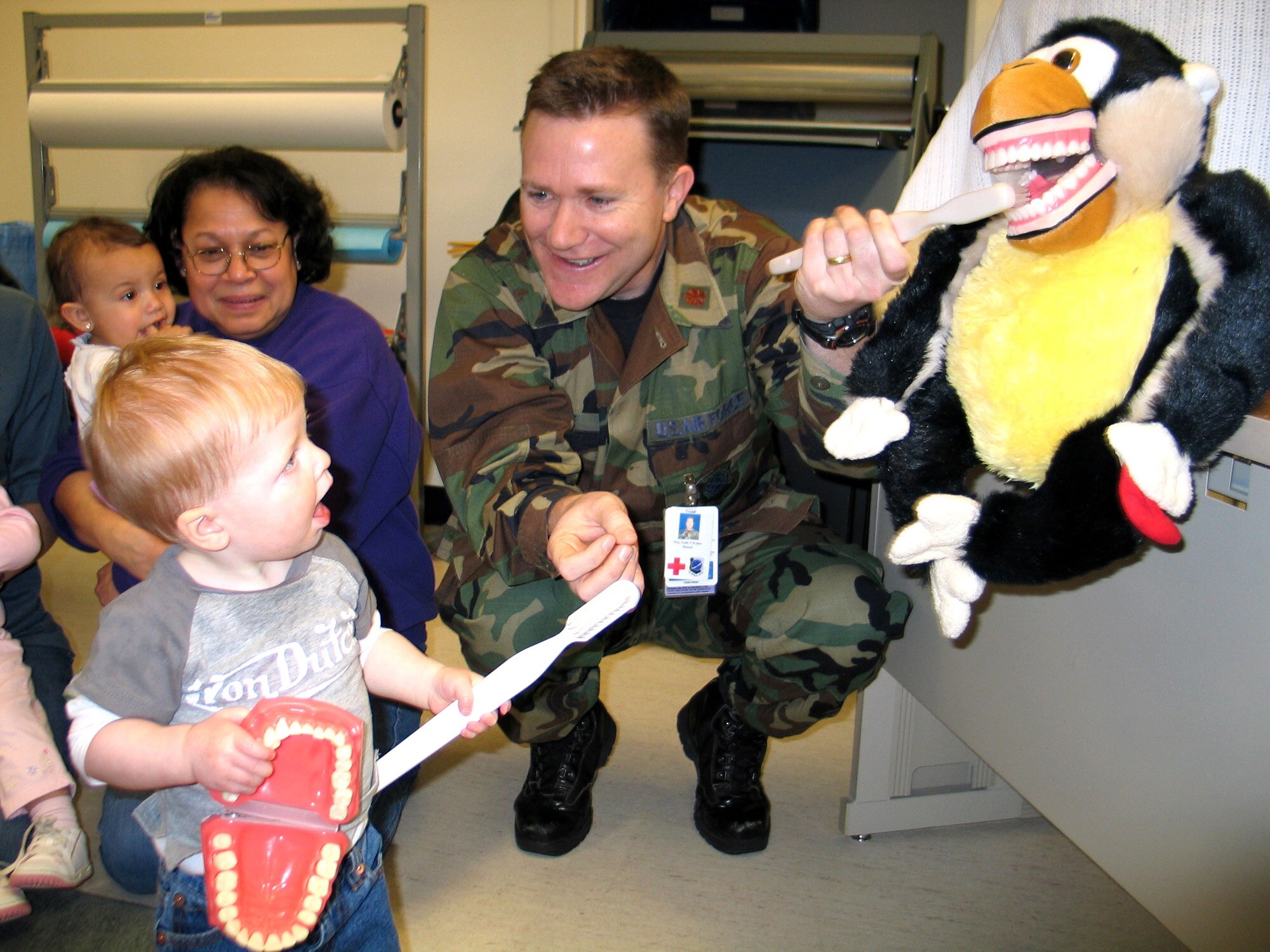 FAIRCHILD AIR FORCE BASE, Wash. -- Maj. Todd Weller, 92nd Dental Squadron, enlists the help of Justin Brown, 15 months, to brush Mojo the Monkey's teeth Tuesday at the Child Development Center. Justin is the son of Tech. Sgt. Jaime Brown, 22nd Training Squadron, and Staff Sgt. John Brown, 92nd Maintenance Operations Squadron. The dental team is making numerous trips to the CDC and base elementary schools this month in honor of National Children's Dental Health Month. Topics of education and discussion include brushing and flossing, dental care at home, and diet and nutrition for older children. "We're really trying to get across prevention," said Major Weller. "If you get started now, at this young age, the chances of having healthy teeth as an adult are much higher." (Photo by Staff Sgt. Connie L. Bias)