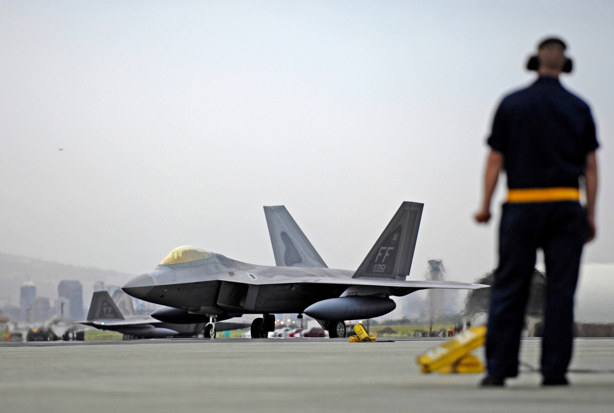 A crew chief waits to marshal a F-22 Raptor to its parking spot Feb. 7 at Hickam Air Force Base, Hawaii. The F-22s and more than 250 Airmen from the 27th Fighter Squadron at Langley Air Force Base, Va., are bound for Kadena Air Base, Japan, for the aircraft's first overseas operational deployment. (U.S. Air Force photo/Tech. Sgt. Shane A. Cuomo) 