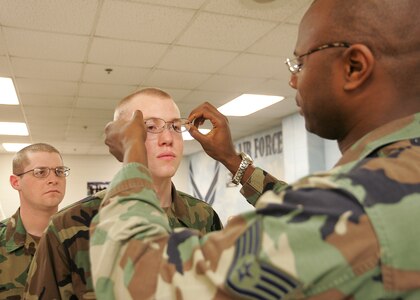 Trainee Brady Fender gets his new frame-of-choice glasses adjusted Feb. 5, 2007, by Staff Sgt. Dedrick Mayers, an optometry journeyman in the 37th Aerospace Medicine Squadron. Waiting for an adjustment is Ian Bowers, a fellow trainee in Flight 189, 331st Training Squadron. In a new initiative by Brig. Gen. Darrell Jones, then the 37th Training Wing commander at Lackland Air Force Base, Texas, basic military trainees now are being issued glasses with frames in colors and styles of their own choosing. (USAF photo by Robbin Cresswell)