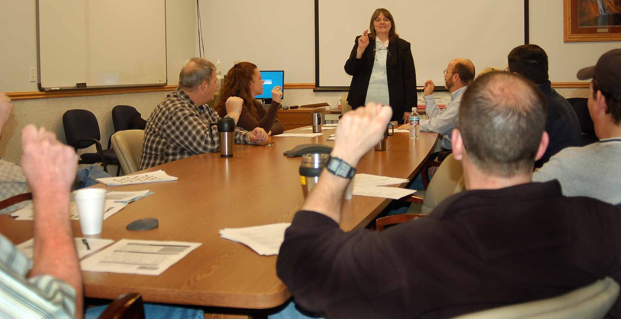 Jean Thomas, standing, the Civilian Personnel Directorate's sign language interpreter for the base and the class instructor, practices the manual alphabet with the students.