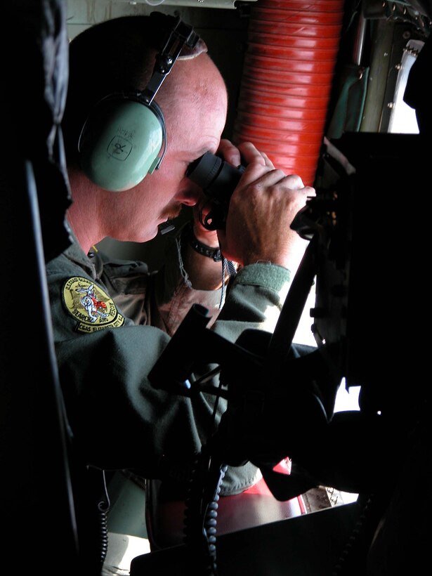 Coast Guard Petty Officer 1st Class Leonard Hoppe, a C-130  loadmaster, peers out the plane's window in hopes of locating a person in the  water. Photo by Sgt. 1st Class Doug Sample