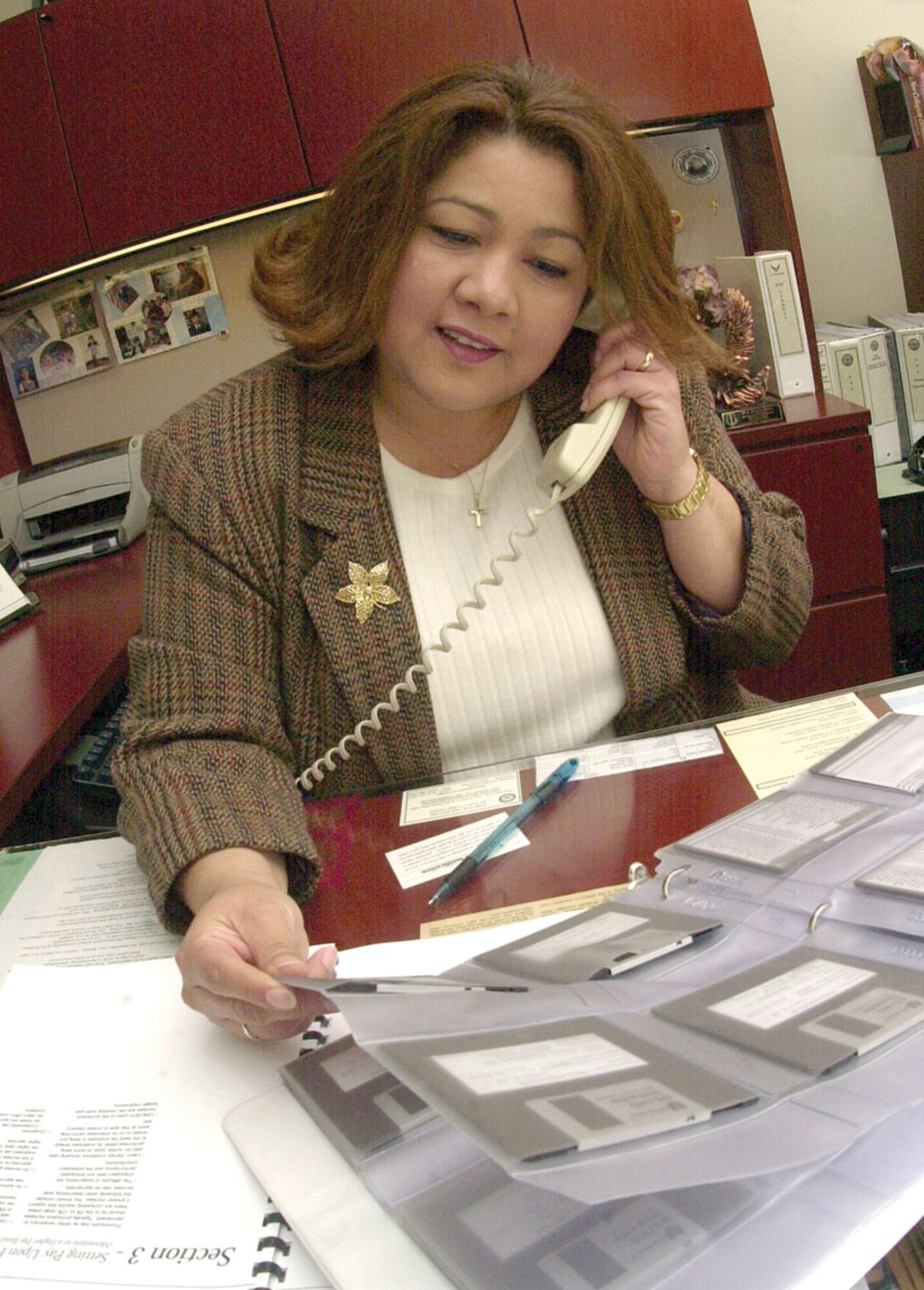 Elizabeth Fuentes looks through a binder while answering a telephone call Wednesday inside her office in the Norma Brown Building. (U.S. Air Force photo by Airman 1st Class Luis Loza Gutierrez)