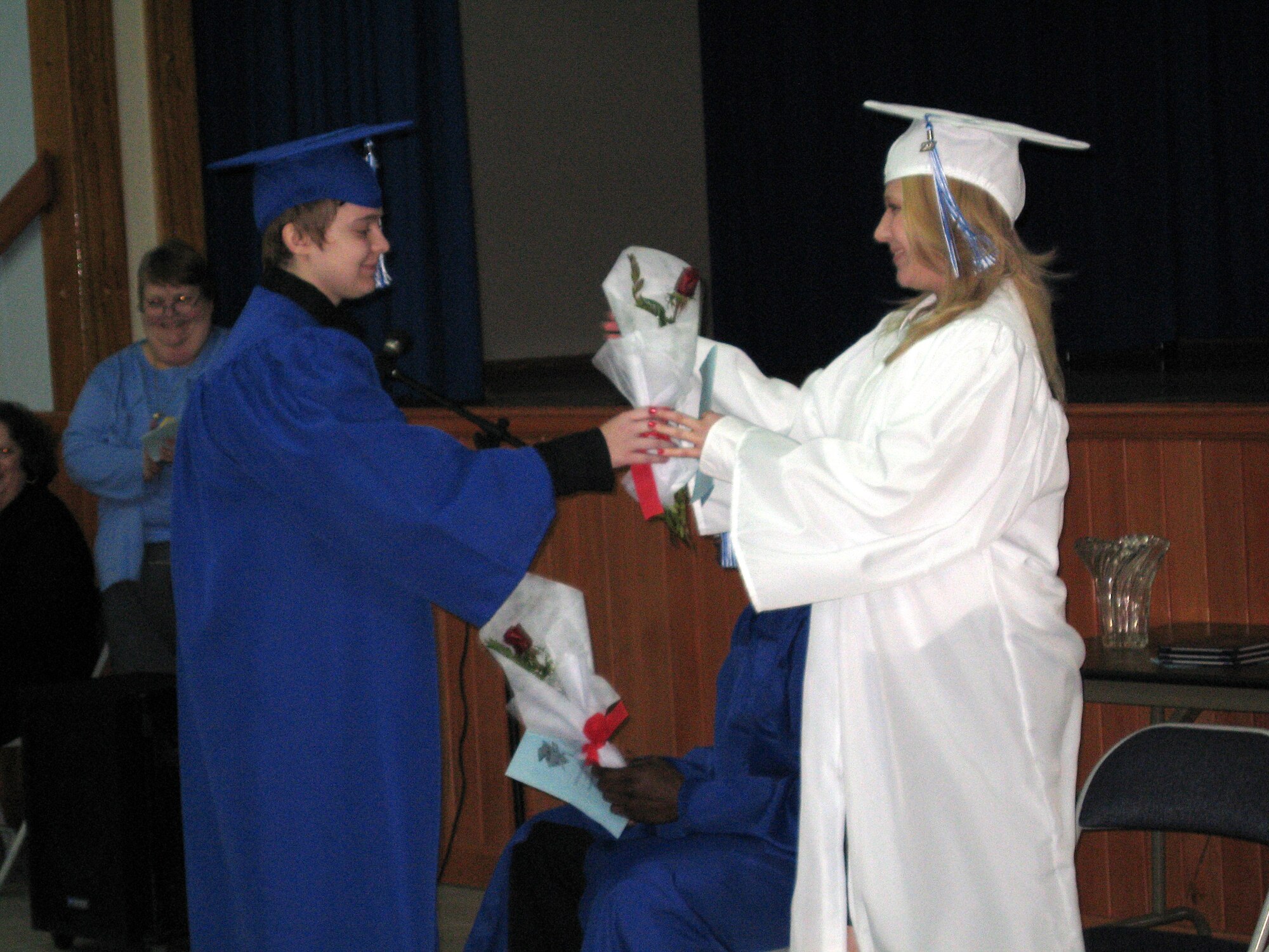 Kristen Lynn Stamper, (left), hands Nicole Marie Smith, (right), and Jeffrey Douglas McWaine (seated)  a rose during Incirlik American Schools mid-year commencement ceremony Feb. 8. (U.S. Air Force photo by Senior Airman Patrice Clarke)