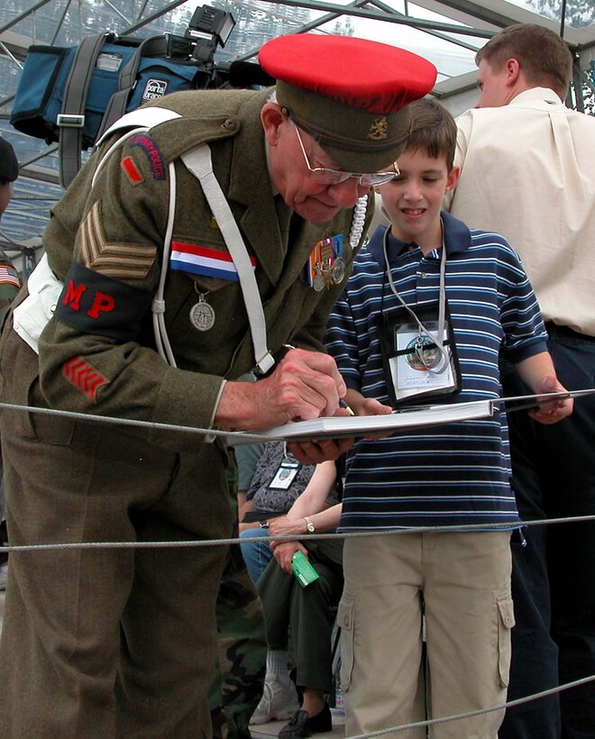 A British veteran of D-Day -- and still able to wear his old  military police uniform -- signs an autograph for a young American during a  tribute to airborne vets at Sainte- Mere-Eglise, France, June 5, on the 60th  anniversary of the Allied jump into the area to liberate the country from the  Germans. Photo by Jim Garamone