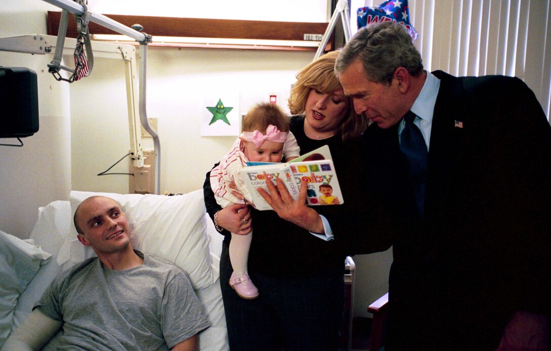 President George W. Bush reads a baby book with U.S. Army  Reservist First Lieutenant Brandan Mueller of Webster Groves, Mo., his wife  Amanda, and their daughter Abigail at Walter Reed Army Medical Center in  Washington, D.C., Friday, March 19, 2004. Lt. Mueller was injured while serving  in Operation Iraqi Freedom. White House photo by Eric Draper.