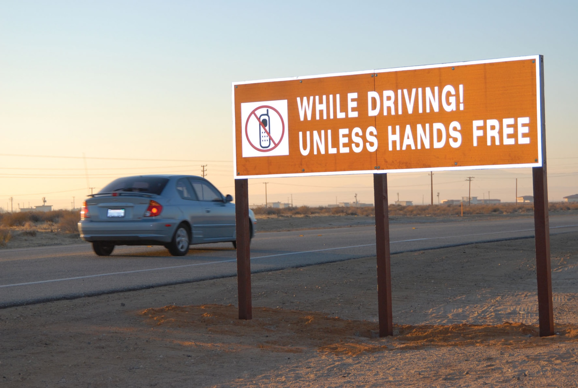 A car passes by a new larger cell phone usage reminder sign at North Gate. The 95th Security Forces Squadron posted the new signs on the base's entrances to better inform the Edwards community and their guests about the base's cellphone policy. (Photo by Senior Airman Jason Hernandez)