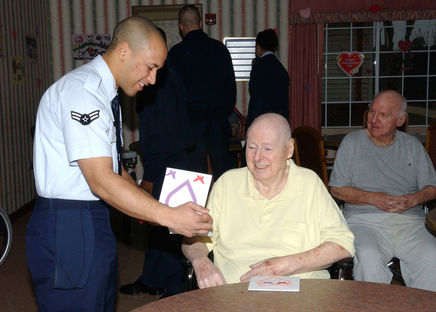 Airman Brandon Glover, 93rd Intelligence Squadron at Lackland Air Force Base, Texas, hands Tom Fuhrman a Valentine's Day card made by two elementary classes in the Lackland Independent School District. Mr. Fuhrman, an Air Force veteran at the Frank M. Tejeda Texas State Veterans' Home in Floresville, and the other 147 residents were visited by approximately 80 members of Team Lackland on Valentine's morning. (USAF photo by Alan Boedeker)                               