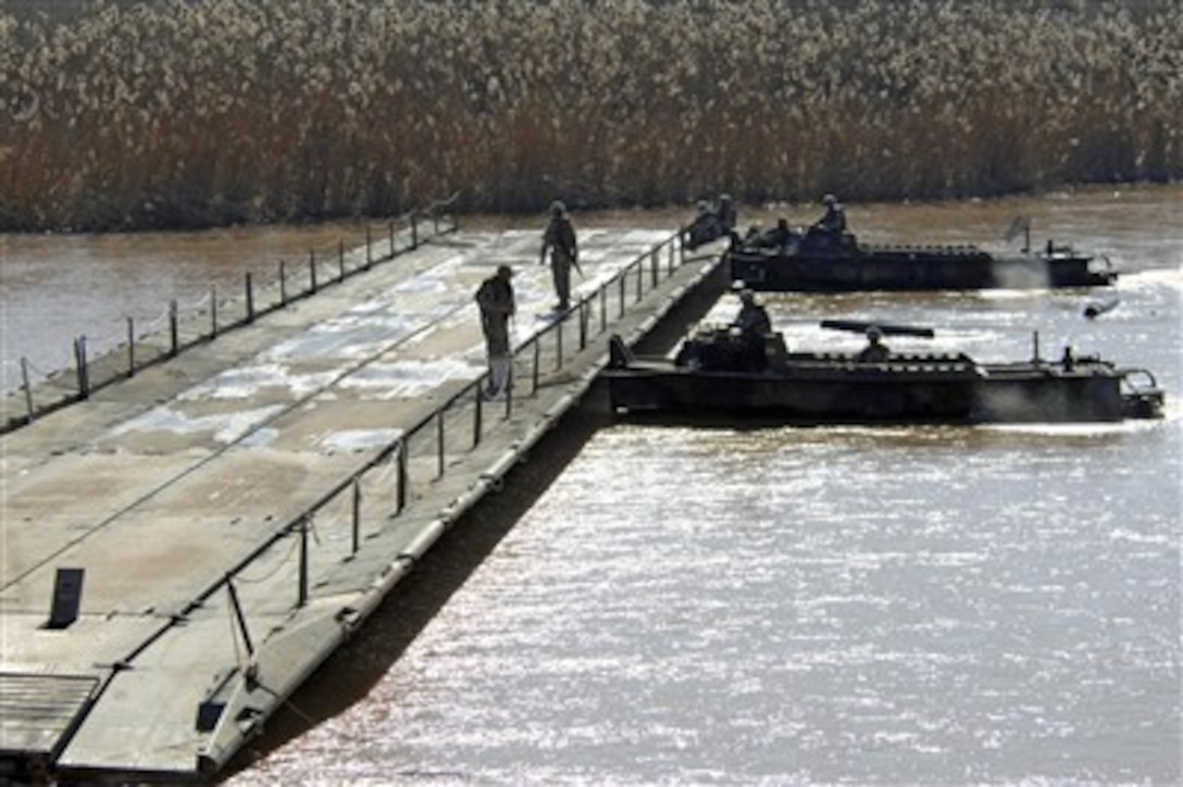 A team of build boats from the 502nd Multi-role Bridge Company, 1st Armor Division, push a newly assembled assault float bridge section upstream outside Camp Taji, Iraq, on Feb. 11, 2007.  