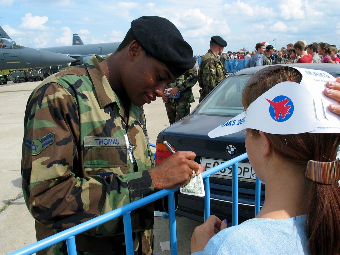 Airman 1st Class Dekota Thompson, with the  569th Security Forces Squadron, signs a U.S. dollar bill  for a Russian girl at the 6th Moscow Aviation and Space  Show Aug. 24. Thompson was one of 24 security forces  members from Ramstein Air Base, Germany, augmenting Russian  special forces to provide security for U.S. aircraft at the  air show. Photo by Master Sgt. Kenneth Fidler, USAF.