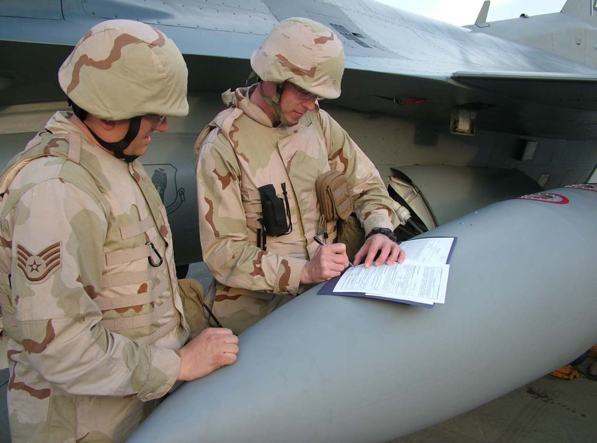 070215--BALAD AIR BASE, Iraq -- Staff Sgt. Jackie Price, 332nd Expeditionary Aircraft Maintenance Squadron, watches as Capt. Jeffrey Campbell, 332nd EAMXS, signs his re-enlistment paperwork Feb. 15 on the flightline. Both Airmen are deployed from the 35th Aircraft Maintenance Squadron at Misawa Air Base, Japan. (U.S. Air Force photo by Senior Master Sgt. Dave Myette) 