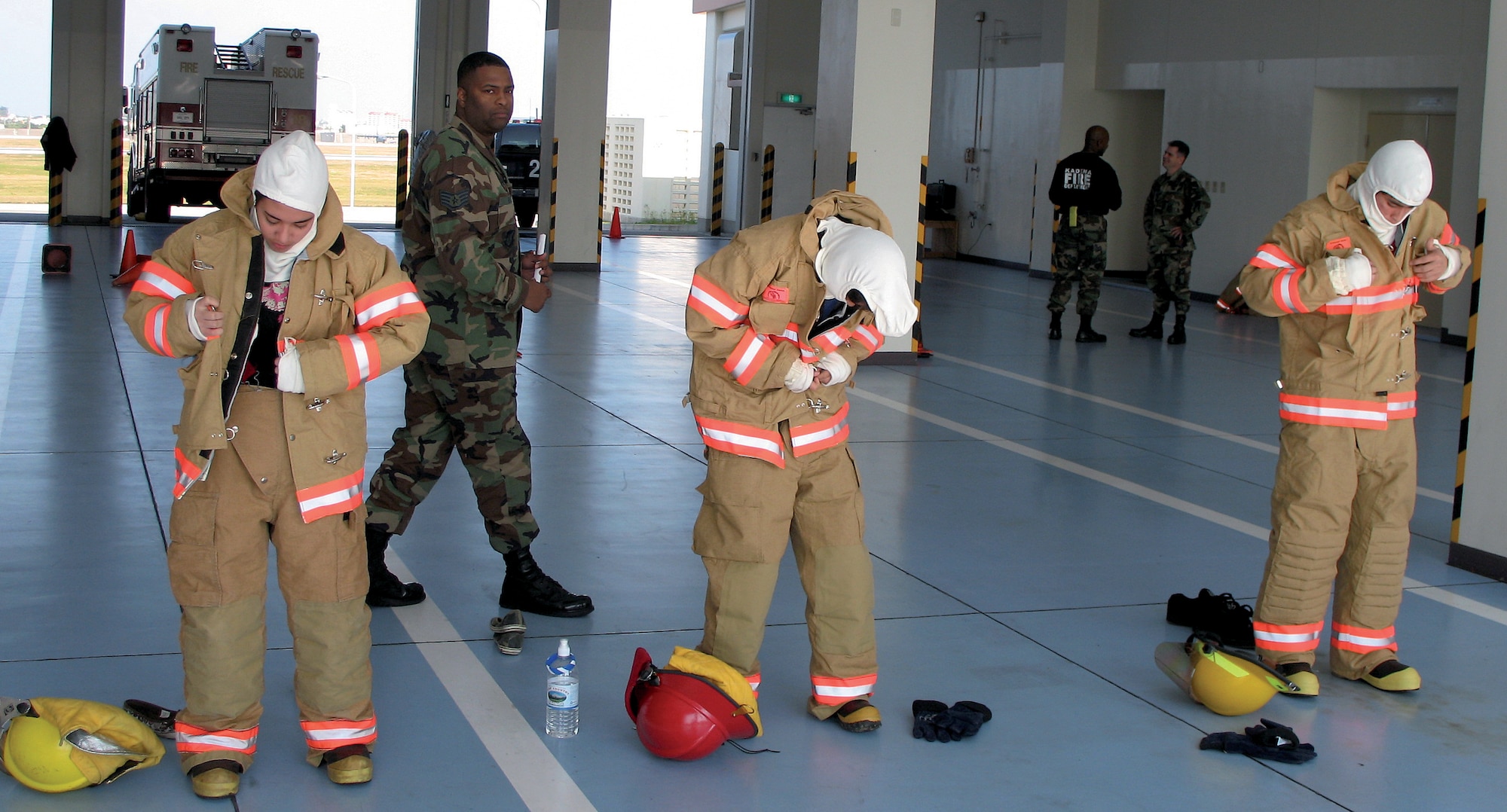 KADENA AIR BASE, Japan -- Students from Kadena High School's Shadow Day program perform a "bunker drill" at the 18th Civil Engineer Squadron Fire Department Feb. 8. Staff Sgt. Deron Branch, 18th CES, tests the students' ability to put on all required fire-fighting gear in under one minute. (U.S. Air Force courtesy photo)
