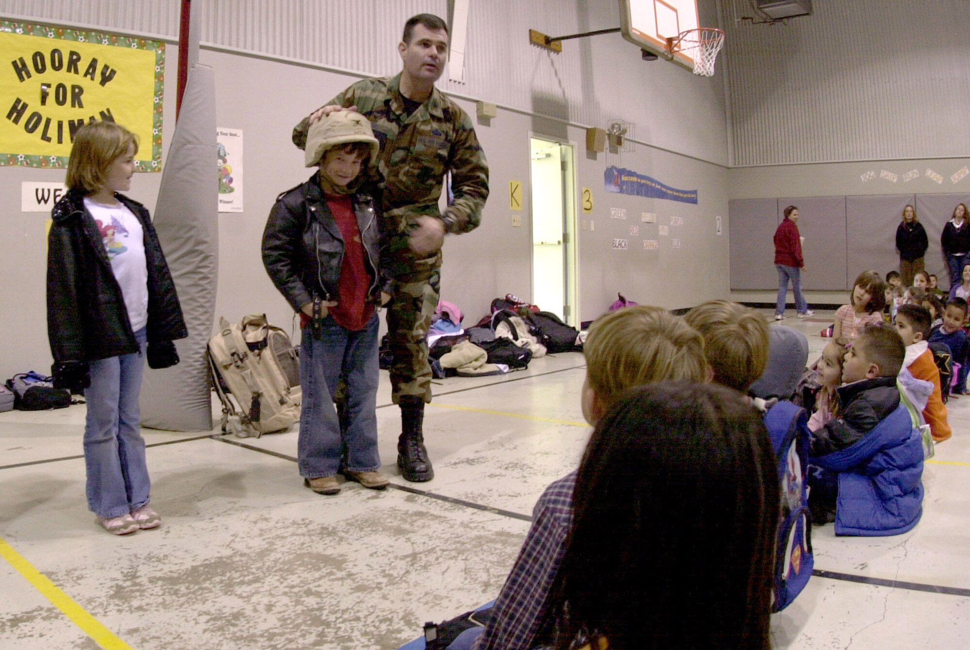 (Left): Col. Scott Bethel, 17th Training Wing commander, helps six-year-old Hunter Herd, a student at Holiman Elementary School, put on a desert camouflage uniform helmet. The student was one of a handful of school children that the commander invited to try out some of his deployment gear. "Our students need great role models in their lives, said Judy Bragg, Holiman’s principal. “To meet a high ranking hero and hear from him the importance of education, leadership, and American pride was a blessing," Judy Bragg, Holiman Elementary School principal said. Col. Bethel was invited as part of a joint program between the school and Paul Ann Baptist Church. Called Project Impact, the program aims to enhance the lives of the school children through special presentations and encouraging words from motivational speakers. (U.S. Air Force photo by Airman 1st Class Luis Loza Gutierrez)