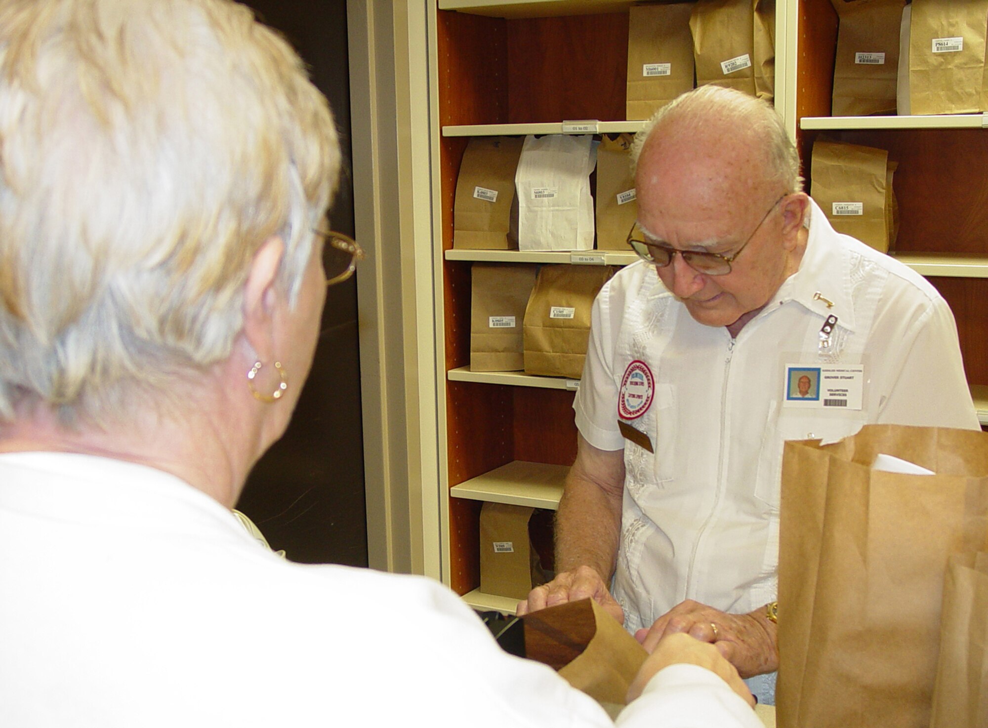 Keesler Medical Center volunteer Grover Stuart hands a prescription to a patient in the main pharmacy.  Mr. Stuart, a retired senior master sergeant, has been providing assistance in the facility for 15 years.  He’s one of approximately 70 people serving as medical center volunteers.   Emily Shelton, volunteer supervisor, said this is fewer than half the people on the rolls before Hurricane Katrina.  More volunteer help is needed as additional services return to the facility, she noted.  For more information, call Mrs. Shelton, 388-6841 or 669-2263.  (U.S. Air Force photo by Steve Pivnick)