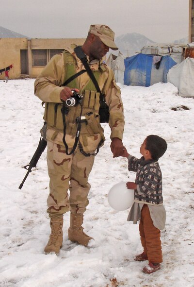 Senior Master Sgt. Darren James holds a refugee child’s hand at Dar ol Aman refugee camp near Kabul, Afghanistan. Sergeant James and his unit delivered 1,000 pounds of food, clothing, school and medical supplies to the camp two to three times per month. (U.S. Air Force photo/Senior Master Sgt. Willian W. Cole)                         