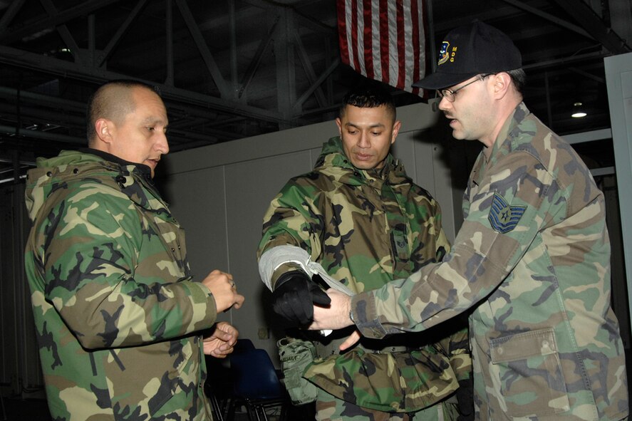 HANSCOM AFB, Mass. -- Tech. Sgt. Robert Cyr, Hanscom Self-Aid and Buddy Care adviser, demonstrates the proper way to wrap an Israeli bandage with the help of 66th Comptroller Squadron personnel Staff Sgt. Robert Mebane and Tech. Sgt. Jose Carrillo. The bandage is among the items included in the Individual First Aid Kit. SABC information begins on page 177 in the Airman’s Manual. U.S. Air Force photo by Linda LaBonte Britt
