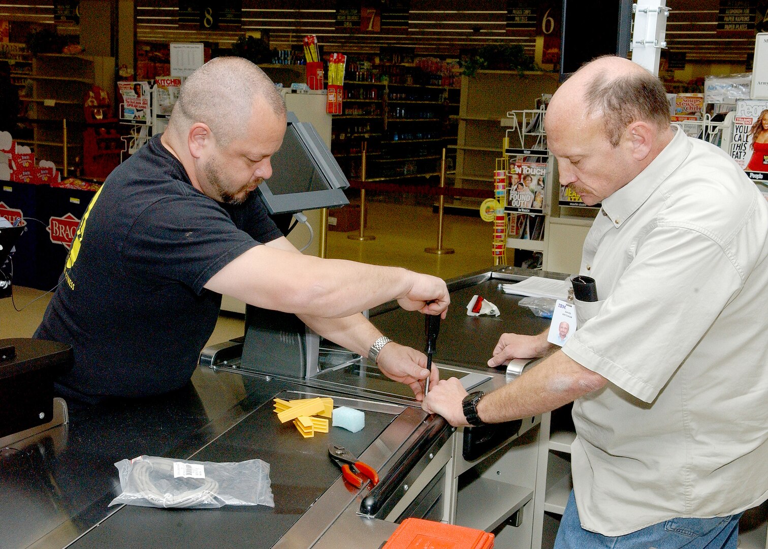 Robert Goupil (left) and David Ketchup from IMB install new registers on Feb. 6 at the commissary on Lackland Air Force Base, Texas. The IMB team replaced the 22 existing registers and installed five additional registers, including using some of the registers to create eight new self-checkout lanes. (USAF photo by Alan Boedeker)