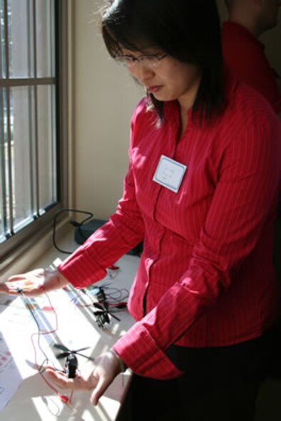 Jin Wang, a material sciences and engineering department second-year doctorate student at the University of Washington, holds a model engine in her left hand being powered by the solar energy collectors held in her right hand. The “Bio-inspired Design of Dye-Sensitized Solar Cells” was on display recently at the Air Force Office of Scientific Research MURI kickoff at the University of Washington. (Air Force photo by William Sharp).