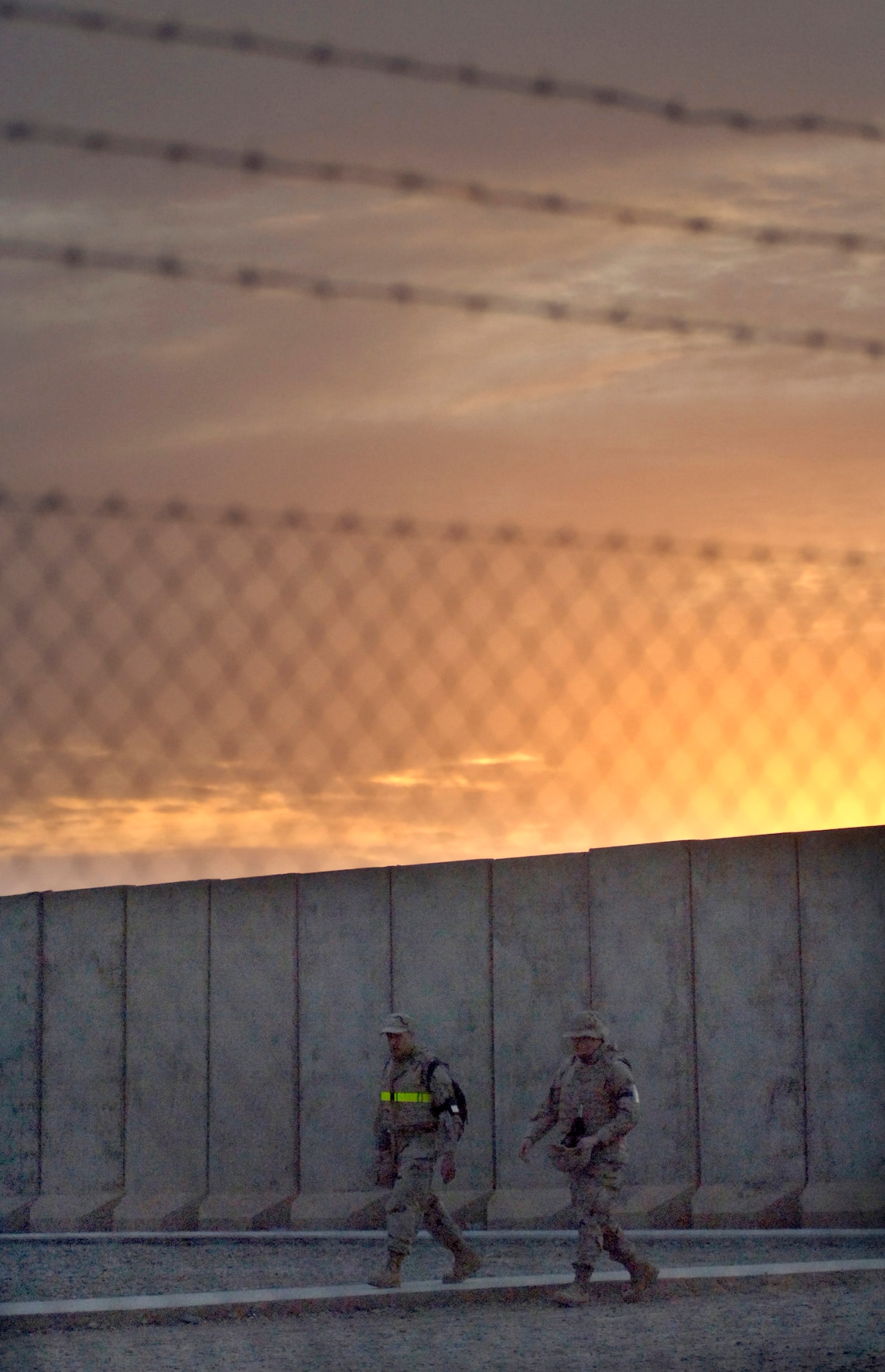 Airmen walk past a wall of T-barriers Feb. 21 after a long duty day at Balad Air Base, Iraq. Most Airmen assigned to the base live in a compound surrounded by towering T-barriers. They act as a line of defense against stray bullets and blast protection from mortar attacks. The weight of the T-barriers varies from four to 17 tons. The T-barriers' purpose is to protect all base facilities. This intricate network of pathways serves as a shield for more than 3,300 Airmen. (U.S. Air Force photo/Tech. Sgt. Cecilio M. Ricardo Jr.)