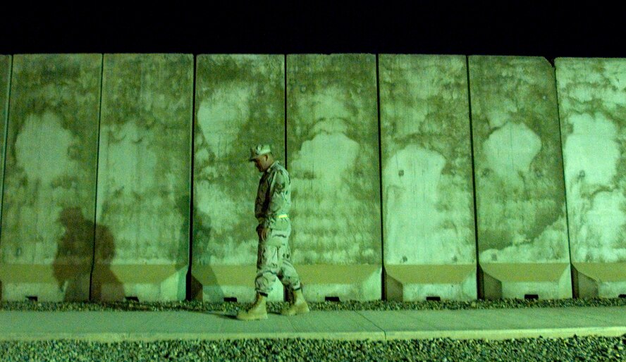 An Airman walks back to his room Feb. 21 after a long duty day at Balad Air Base, Iraq.  Most Airmen assigned to the base live in a compound that is surrounded by towering T-barriers.  They act as a line of defense against stray bullets and blast protection from mortar attacks.  The weight of the T-barriers varies from four to 17 tons.  The T-barriers' purpose is to protect all base facilities.  An  intricate network of pathways serves as a shield for more than 3,300 Airmen. (U.S. Air Force photo/Tech. Sgt. Cecilio M. Ricardo Jr.)
