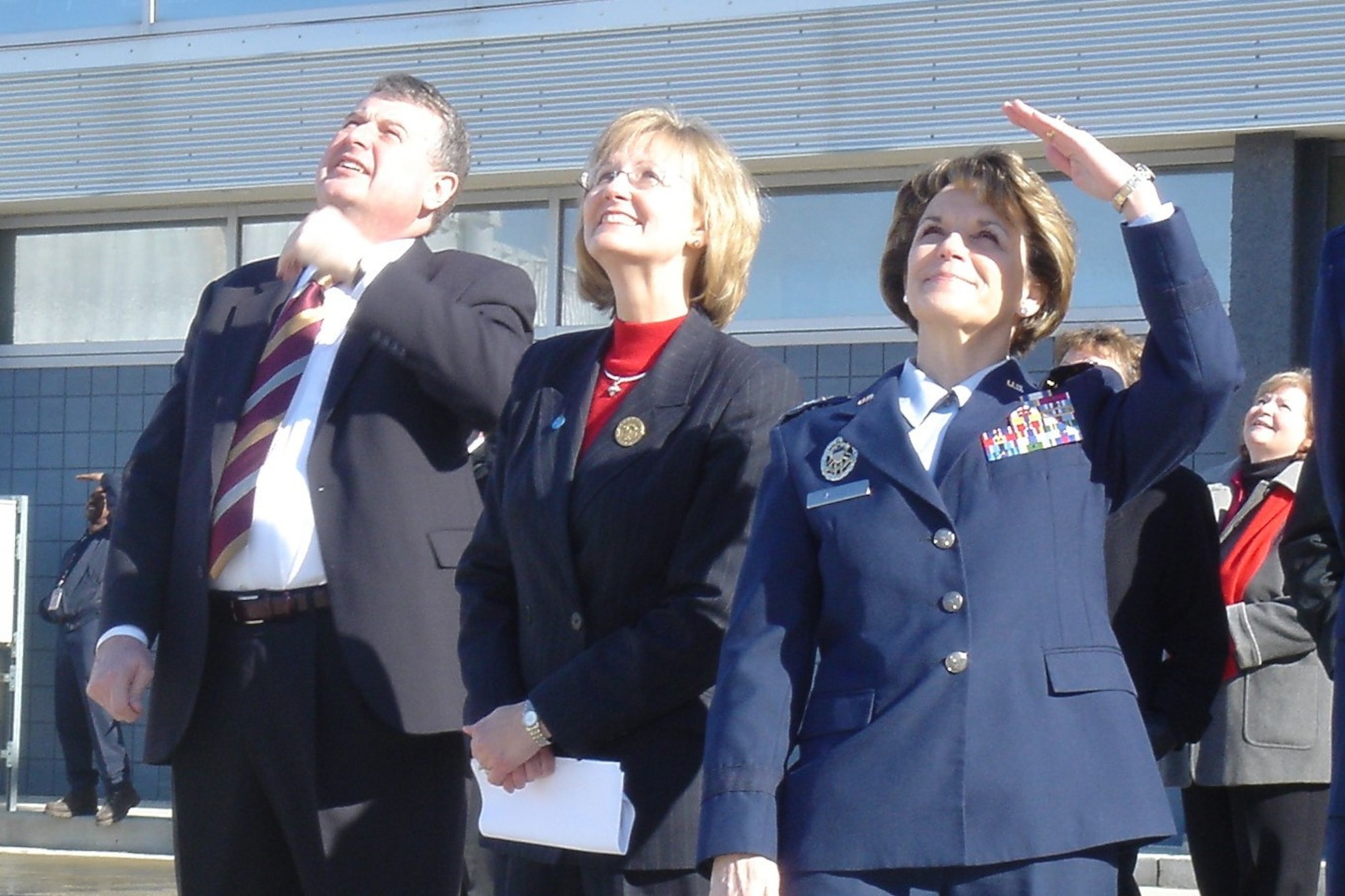 Lt. Gen. Terry Gabreski, vice commander of Air Force Materiel Command, along with Paula Brooks, Franklin County Commissioner, and Rod Borden, senior vice president and chief operating officer of the Columbus Regional Airport Authority, gaze skyward during the fly-by of two P-51 Mustangs in Columbus, Ohio. The trio gathered as part of the announcement that Columbus and the Gathering of Mustangs and Legends will host Air Force Heritage Week in September. (Air Force photo)