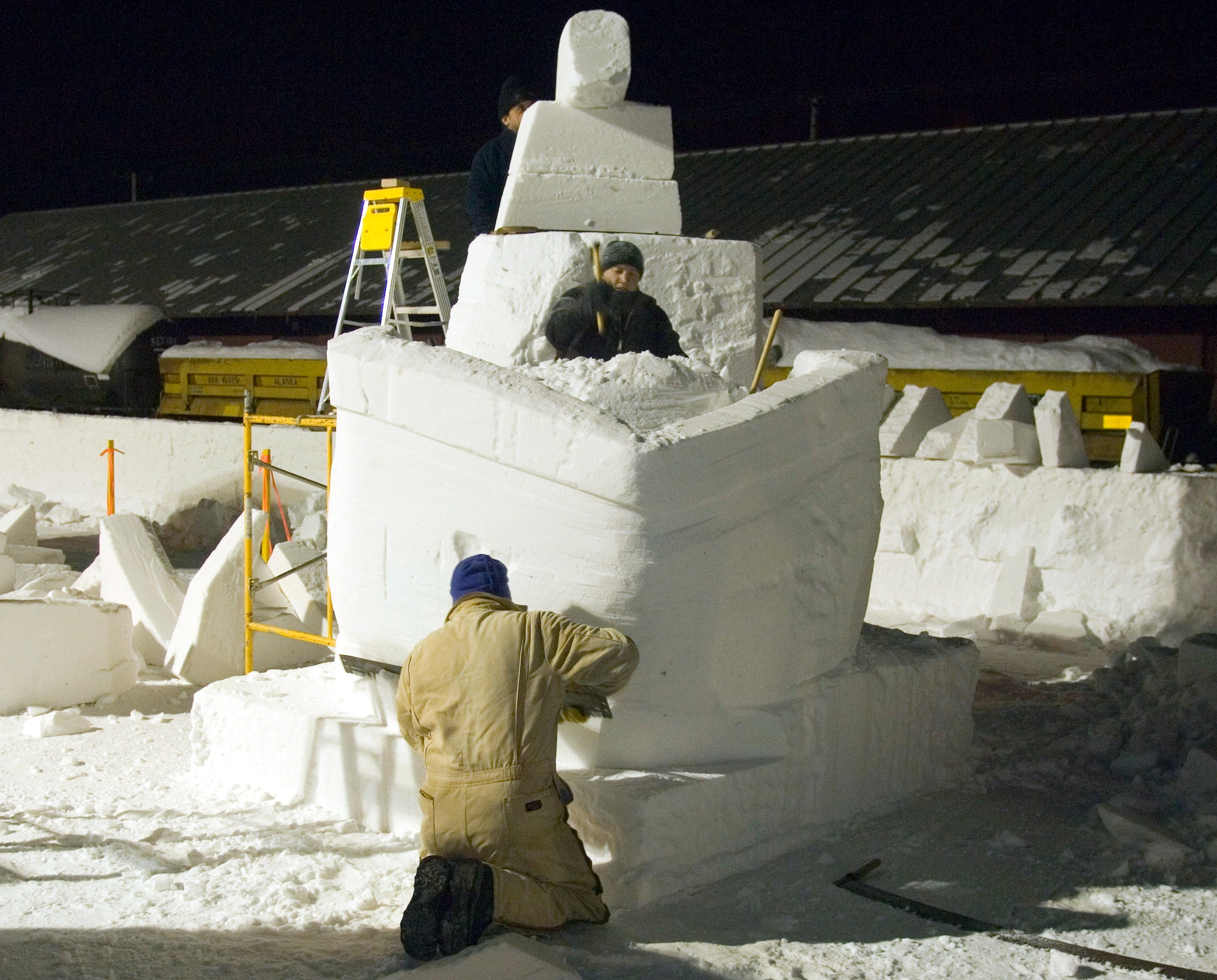 Eric Zimmerman (kneeling), Staff Sgt. Edward Tompkins and Mitchell Manzo (on ladder), comprising the Elmendorf Air Force Base snow sculpting team, work late into the night Feb. 23 carving out a pirate ship during the Anchorage, Alaska, Fur Rendezvous snow sculpture competition.  The team pushed through the exhaustion of freezing temperatures and long hours of labor to vie for a chance to be invited to the 2008 National Snow Sculpting Championship in Lake Geneva, Wis.  (U.S. Air Force photo/Senior Airman Garrett Hothan)