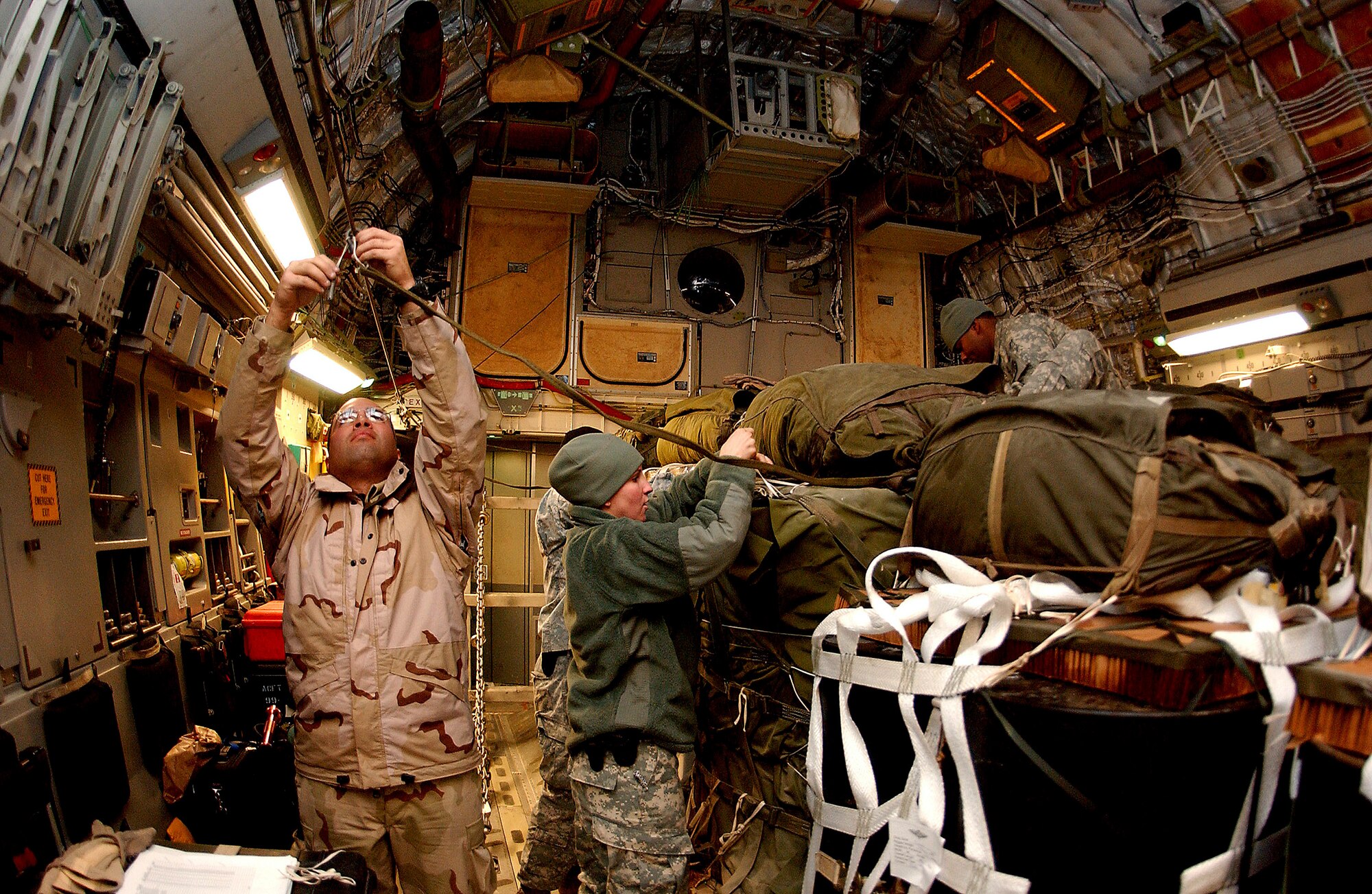 Staff Sgt. Jose Cruz (left) of the 816th Expeditionary Airlift Squadron works with Army Soldiers to tie the drop cords that will release parachutes attached to supply pallets Jan. 2 at Bagram Air Base, Afghanistan. The pallets will be airdropped from a C-17 Globemaster III to servicemembers at remote camps in Afghanistan. (U.S. Air Force photo/Senior Airman Ricky J. Best)
