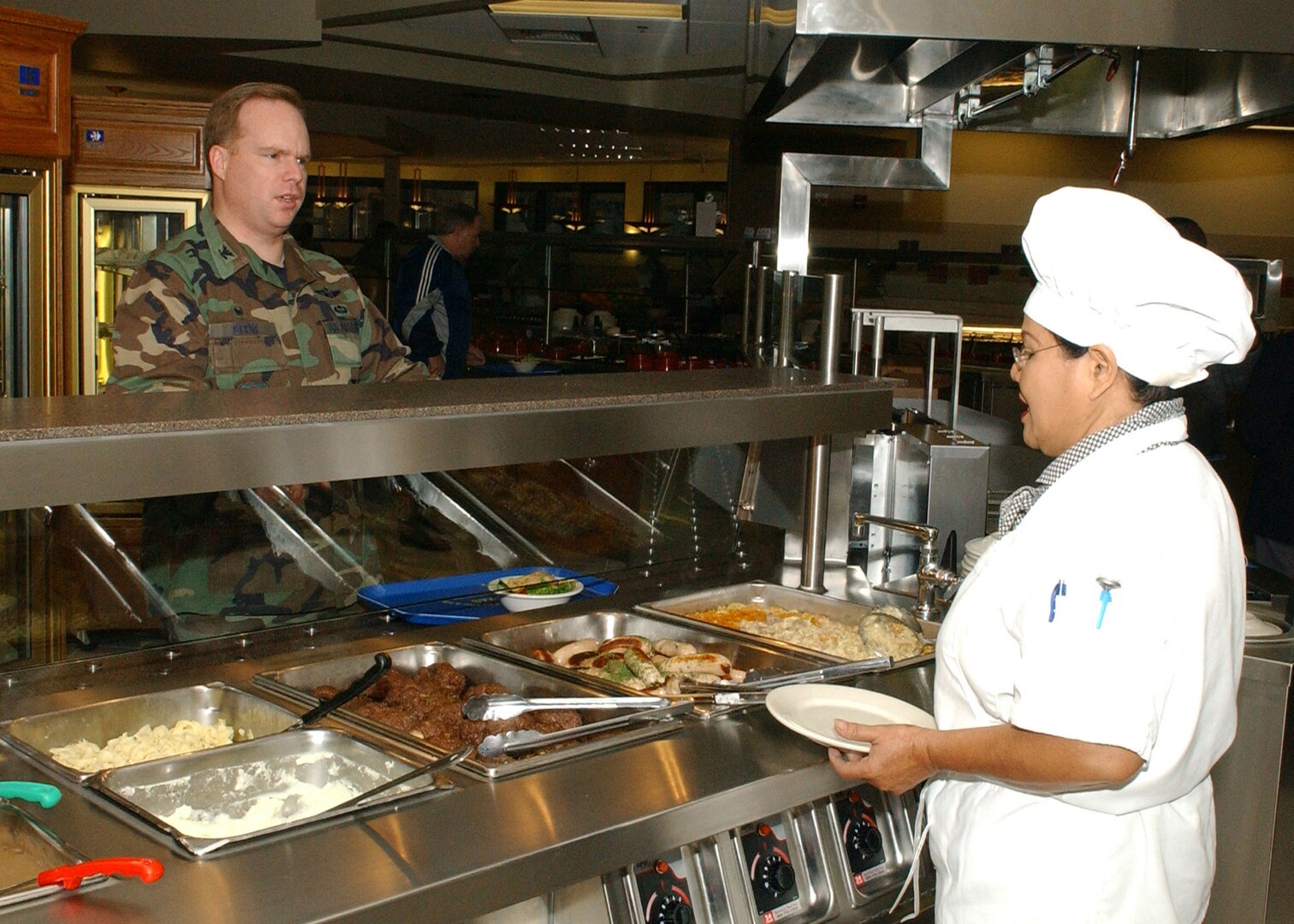 Ratchanee Jones prepares to dress Col. Eric Beene's plate with his entree choice during the dining facilities' opening day Jan. 3. Colonel Beene is the 37th Mission Support Group commander. The dining facility, located on the Lackland Training Annex at Lackland Air Force Base, Texas, mainly serves technical students and instructors from the 342nd, 343rd and 344th Training Squadrons, and members of the 90th Intelligence Squadron. The facility can hold up to 1,500 diners, has four serving lines and three dining areas, and has modern lighting and wooden floors. Construction of the dining facility, which replaced the 35-year-old Medina Inn, is among $60.3 million in major building projects scheduled for opening early this year. (USAF photo by Alan Boedeker)    