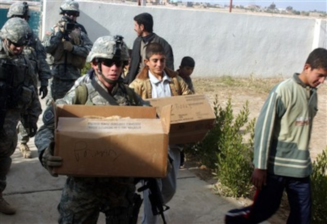 U.S. Army Pvt. Kevin Hardin of Delta Company, 3rd Battalion, 8th Cavalry, helps local children carry school supplies into a primary school in Al Huwaish, Iraq, Dec. 26, 2006. 