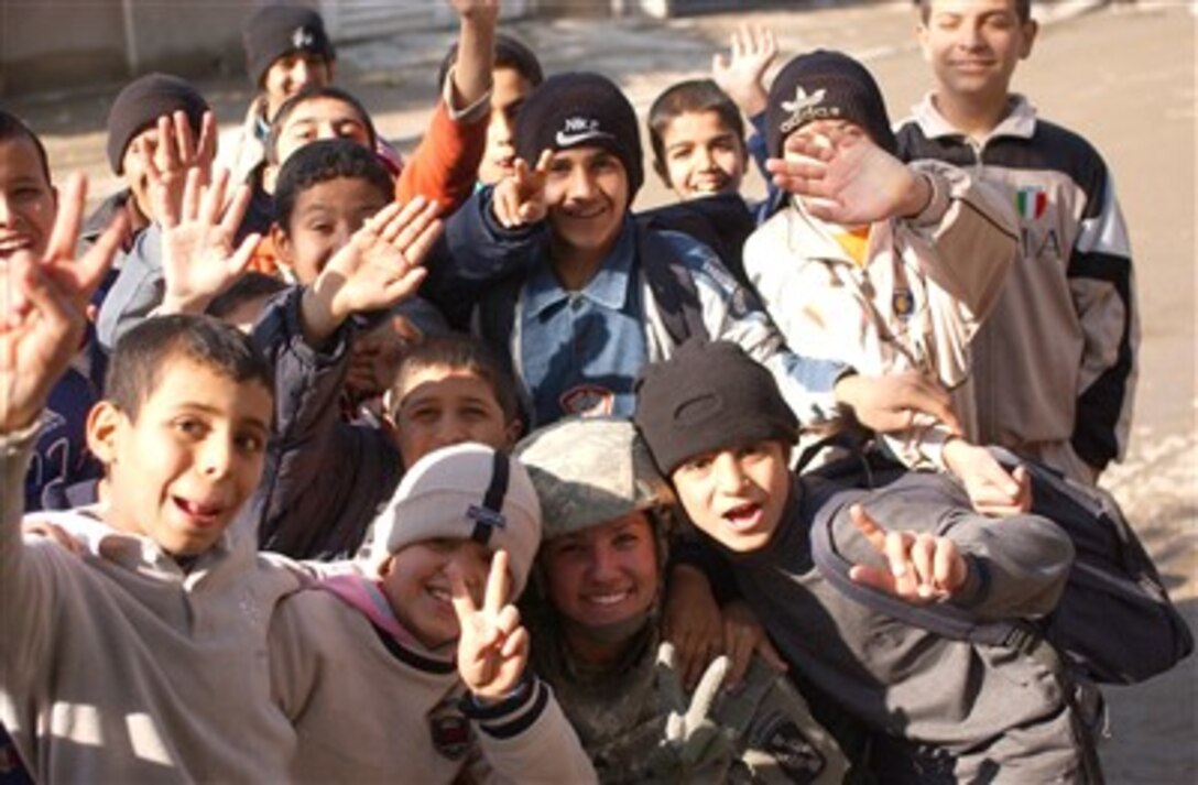 U.S. Army Sgt. Tierney Nowland, from the 982nd Combat Camera Company, poses for a photo with a group of Iraqi children as she documents a cordon and knock operation outside Sadar City, Iraq, Dec. 24, 2006.