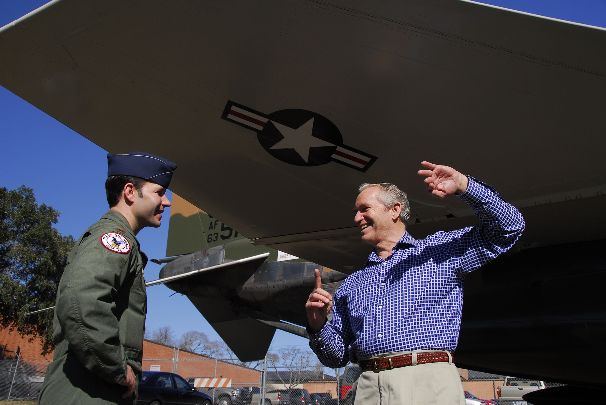 Texas Air National Guard Maj. Jon Stone, a pilot in the 149th Fighter Wing, listens to his father, retired Air Force Col. John Stone, describe flying missions he executed in F-4 aircraft like the static display behind them. Colonel Stone visited the wing on Lackland Air Force Base Jan. 5. (Texas National Guard photo by Senior Master Sgt. Mike Arellano)