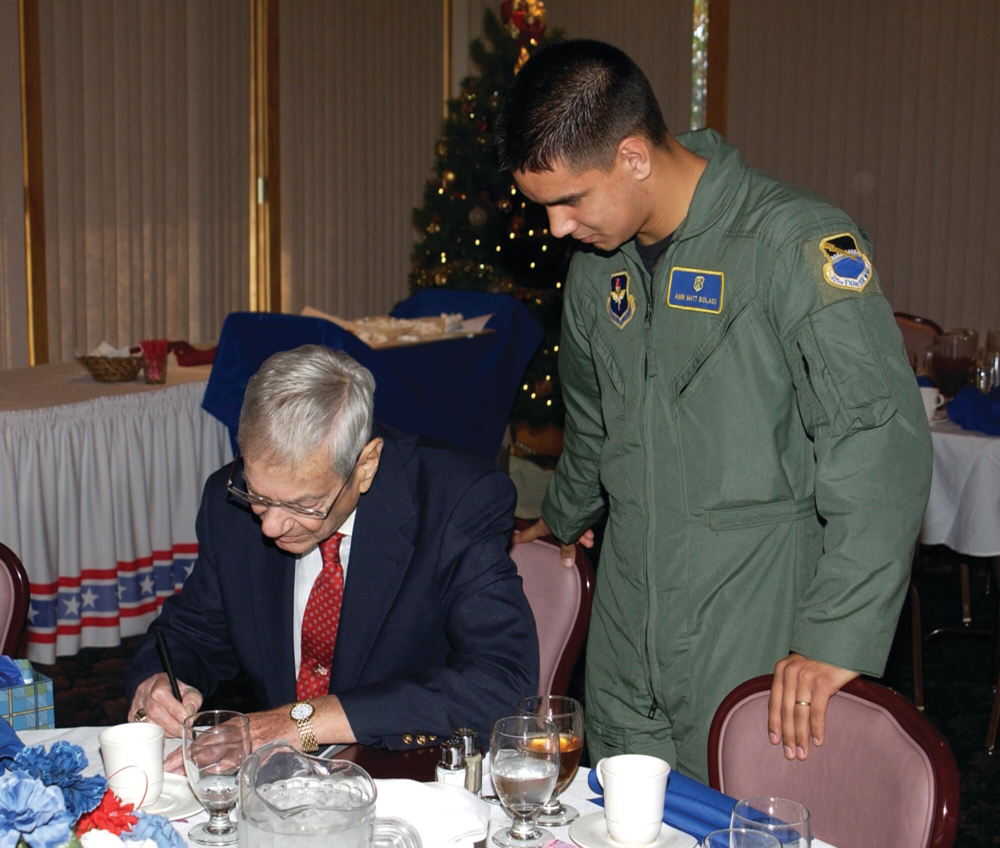 During his 80th birthday celebration here December 2003, retired Chief Master Sgt. of the Air Force Airey signs an autograph for Senior Airman Matthew Bolado, 325th Aeromedical-Dental Squadron. 