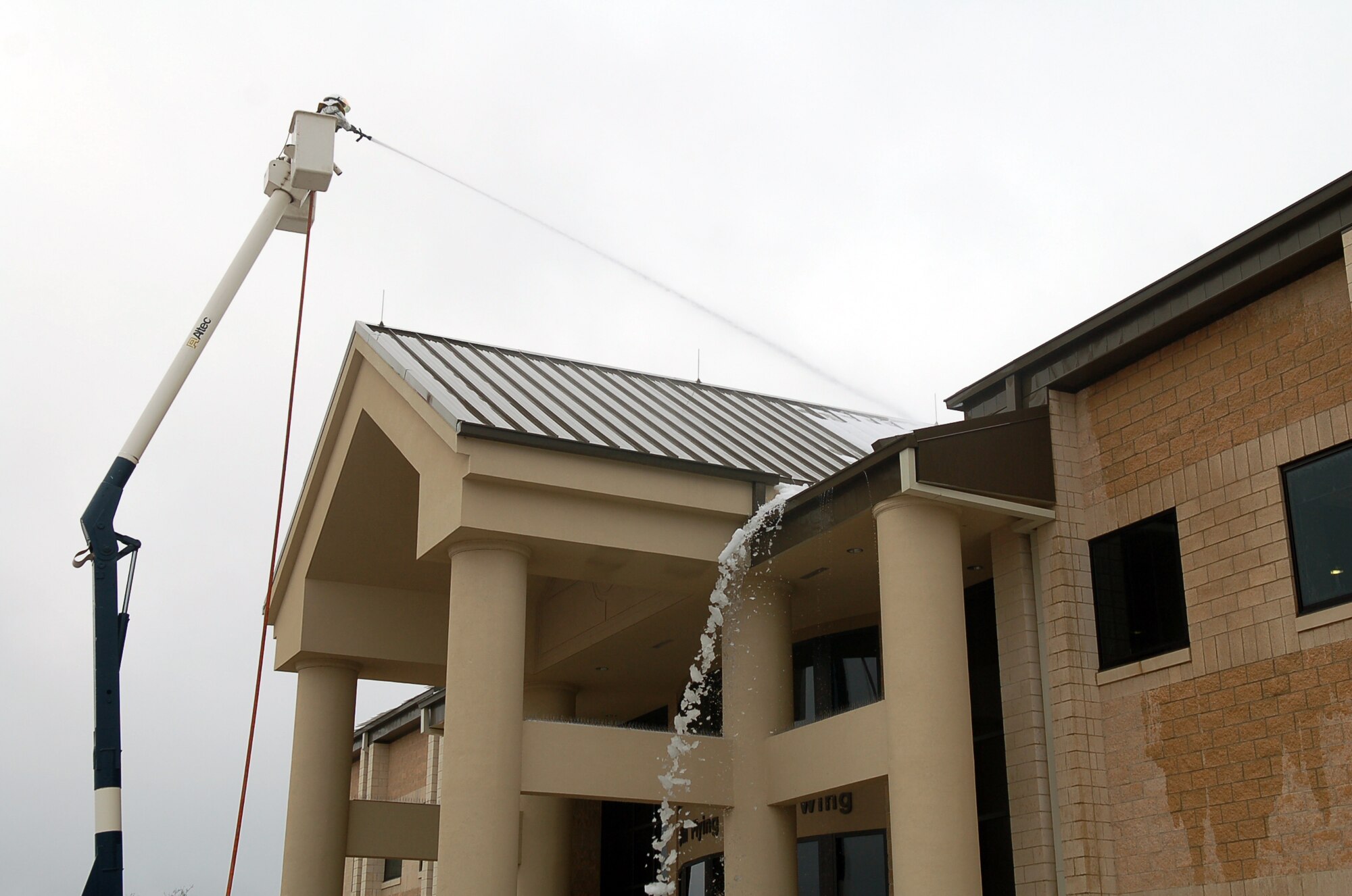 Airman Nicholas Powanda, Laughlin fire department, sprays snow and ice from the roof of the 47th Flying Training Wing headquarters building Thursday.  Since snow and ice are unusual this far south, most buildings in the area are not equipped with protective measures to keep heavy snow from falling off roofs onto walkways and entryways.  The fire department was called to help remove these hazards once they began melting, causing them to fall.  (U.S. Air Force photo by Staff Sgt. Austin May)
