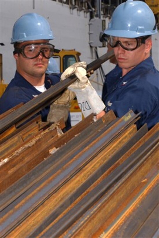 Navy Petty Officers Rocky Toedtemeier (left) and Richard Ellis move pieces of angle-iron to be used for repairs onboard the USS Frank Cable (AS 40) in Santa Rita, Guam, on Jan. 12, 2007.  The Cable, a submarine tender, is in a 4-month phased maintenance availability receiving repairs and upkeep.  