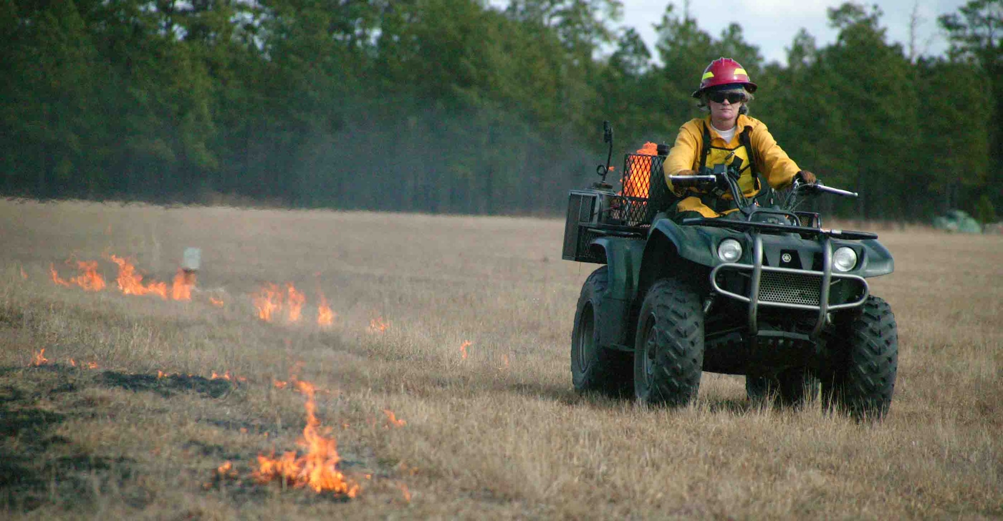 Julie Hovis, 20th CES endangered species manager, drives an all-terrain vehicle igniting the field behind her. The all-terrain vehicle has a torch on the back. A button on the front of the vehicle operates the fuel spray, which sends ignited fuel to the ground. (U.S. Air Force photo/Senior Airman John Gordinier)