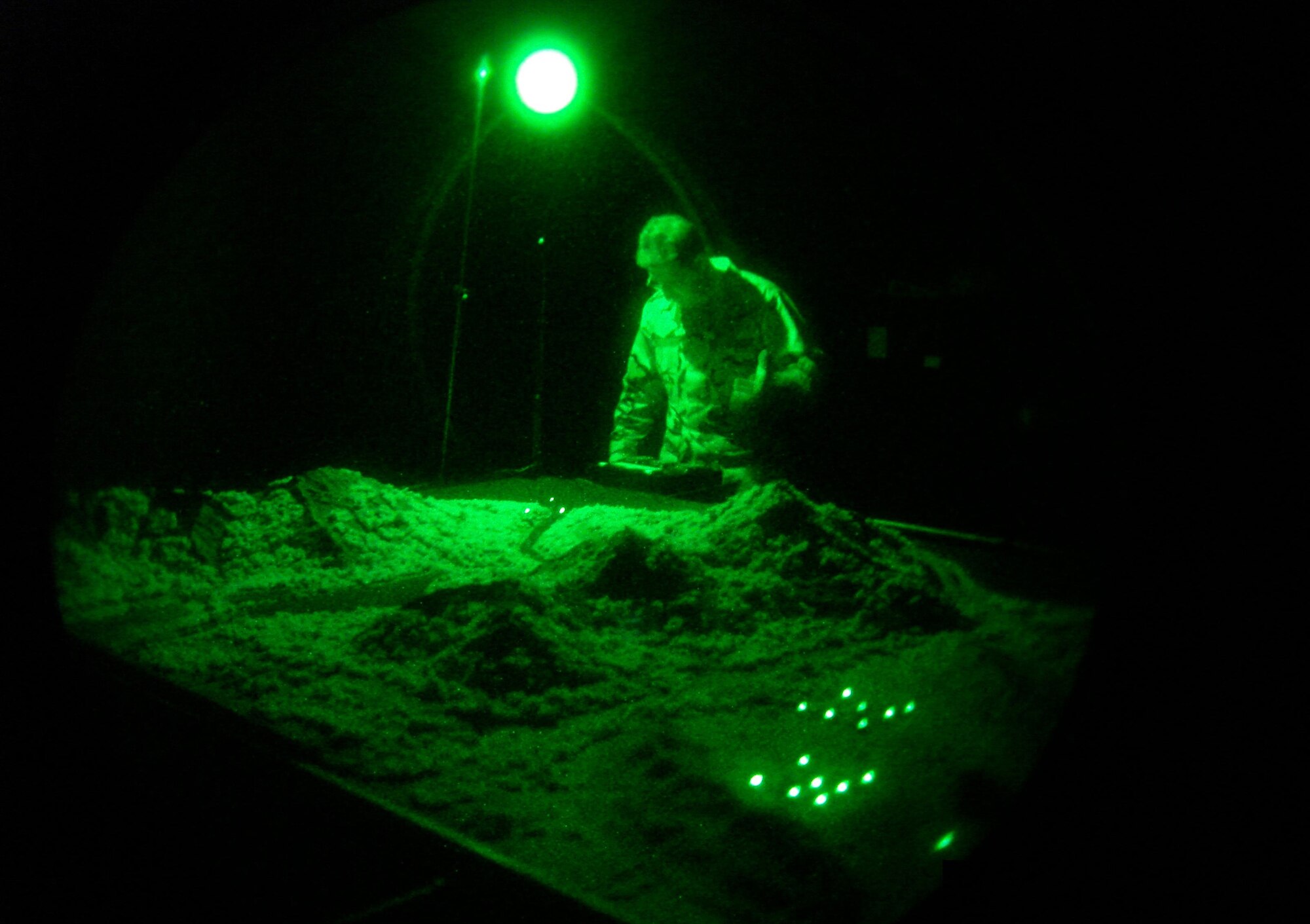 Capt. Tom Massa, Air Force Night Vision Goggle Academic Instructor Course director, adjusts the lighting on the terrain board (a scale model of desert mountain urban environments) in the "nite lab" to demonstrate the effects of shadows, illumination and contrast on NVG visual performance. (U.S. Air Force photo by Capt. Alex Ramos)                                                        